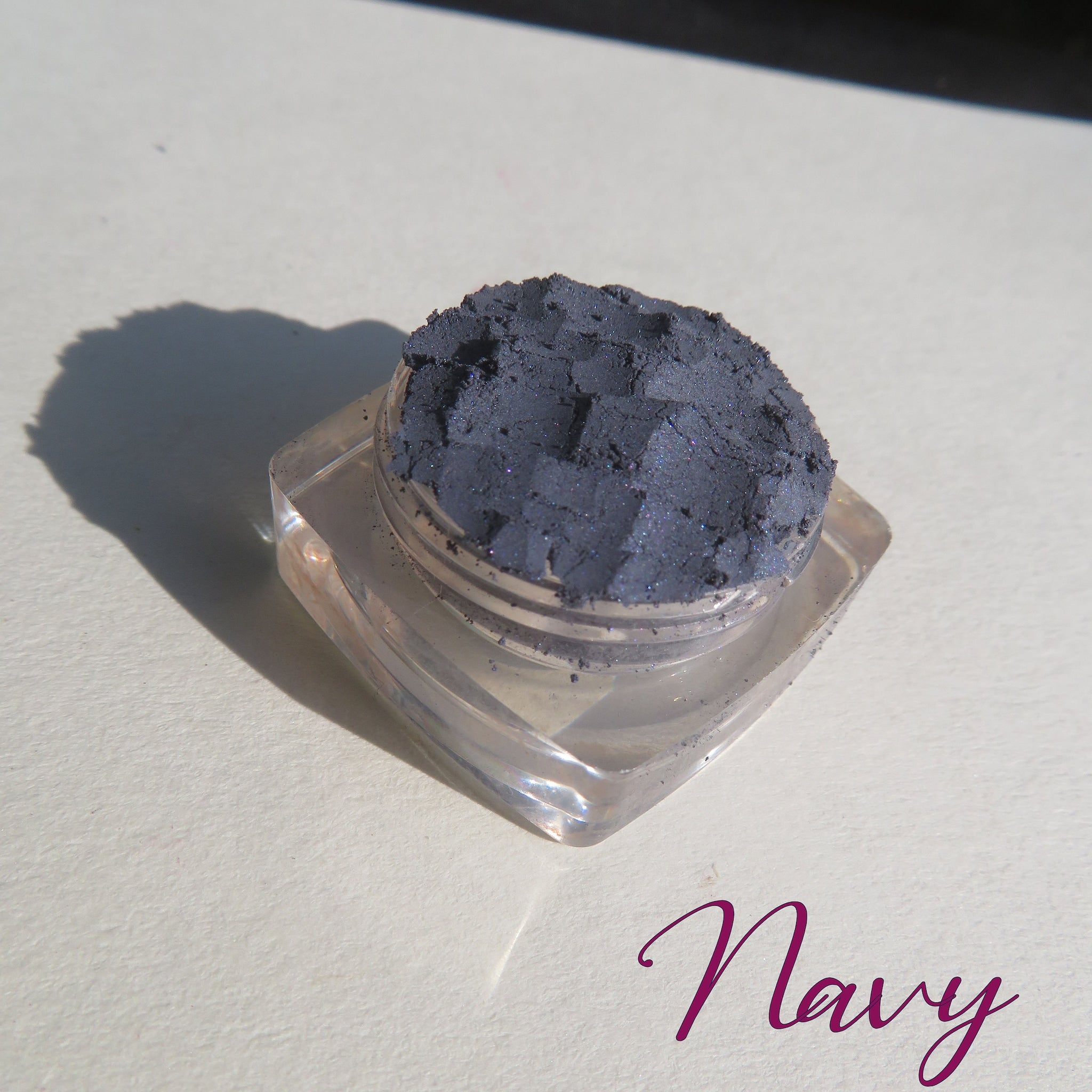 Navy blue shimmer loose powder eyeshadow spilled on marble surface with brush nearby