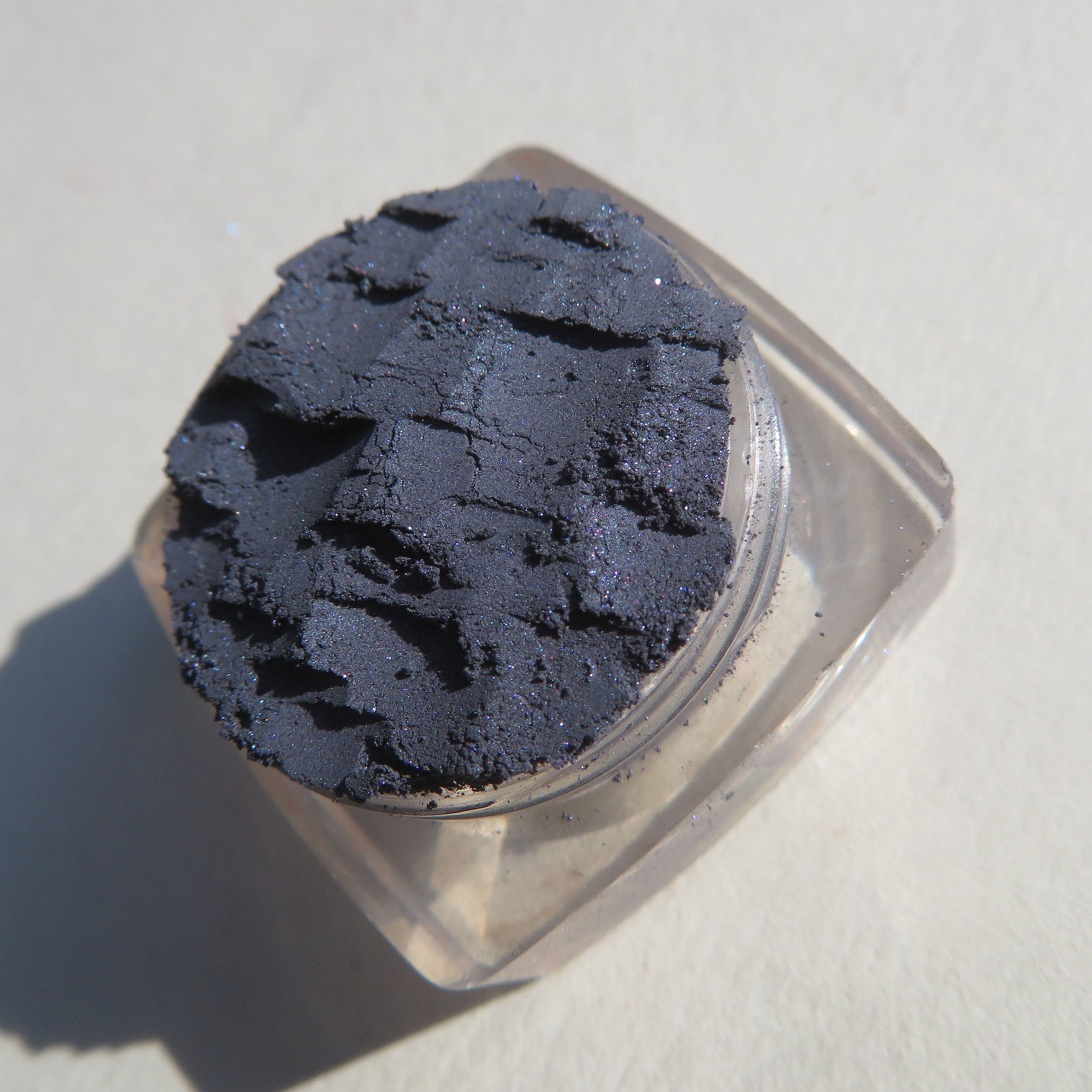 Close-up of navy blue shimmer loose powder eyeshadow with sparkling particles in a textured finish
