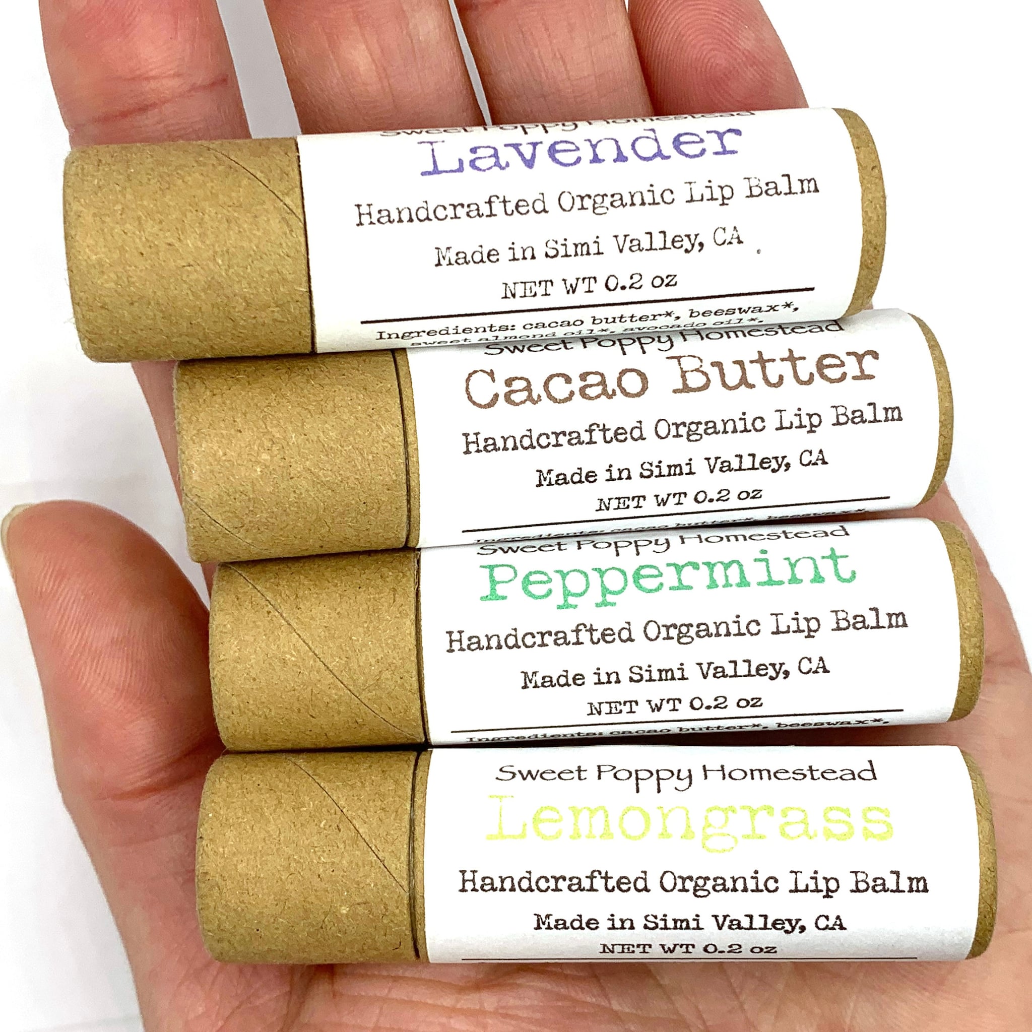 Lip balm tubes in brown cardboard with white labels, held in hand, Sweet Poppy Homestead brand visible