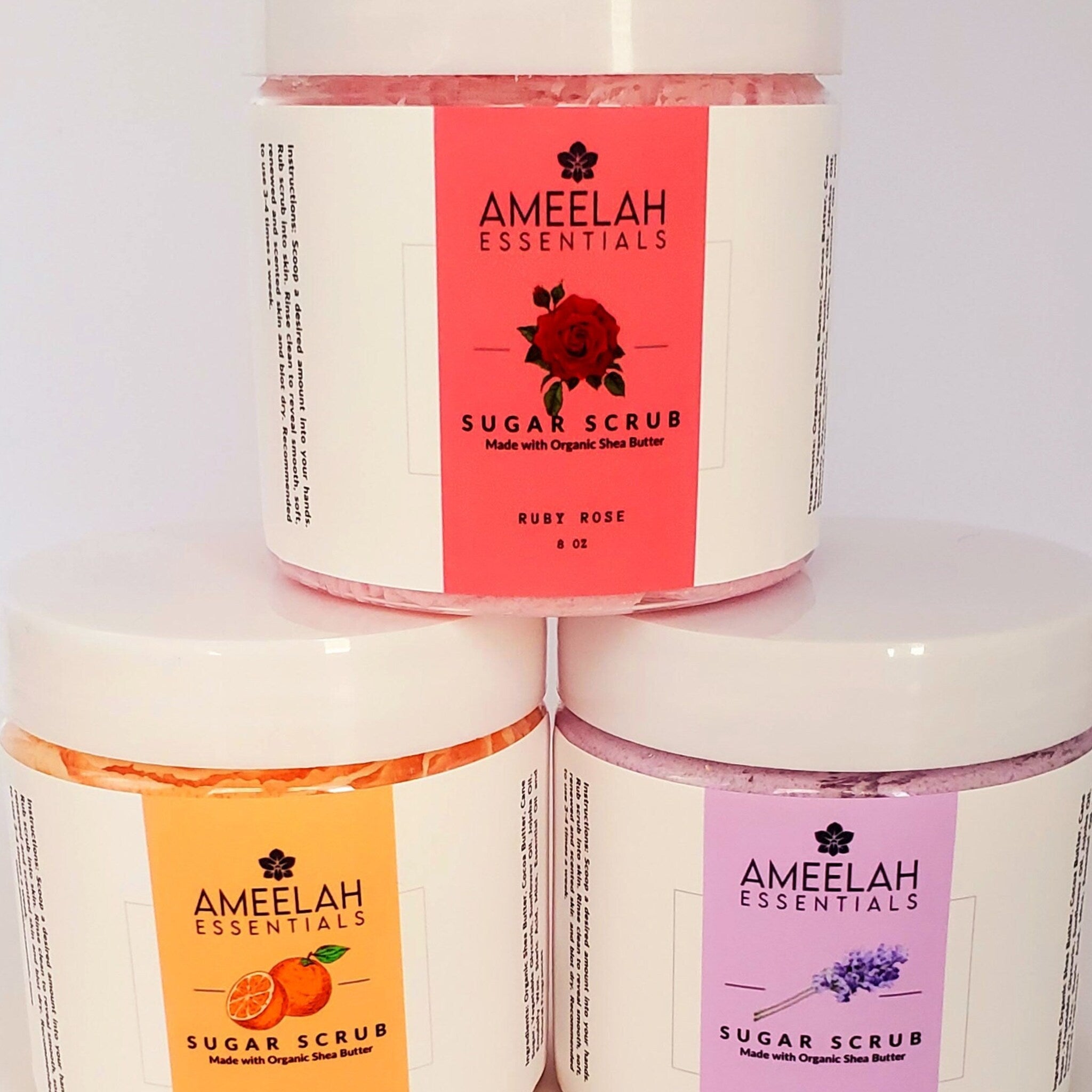 Sugar scrub jars with Ameelah Essentials labels, stacked with white lids and colorful labels