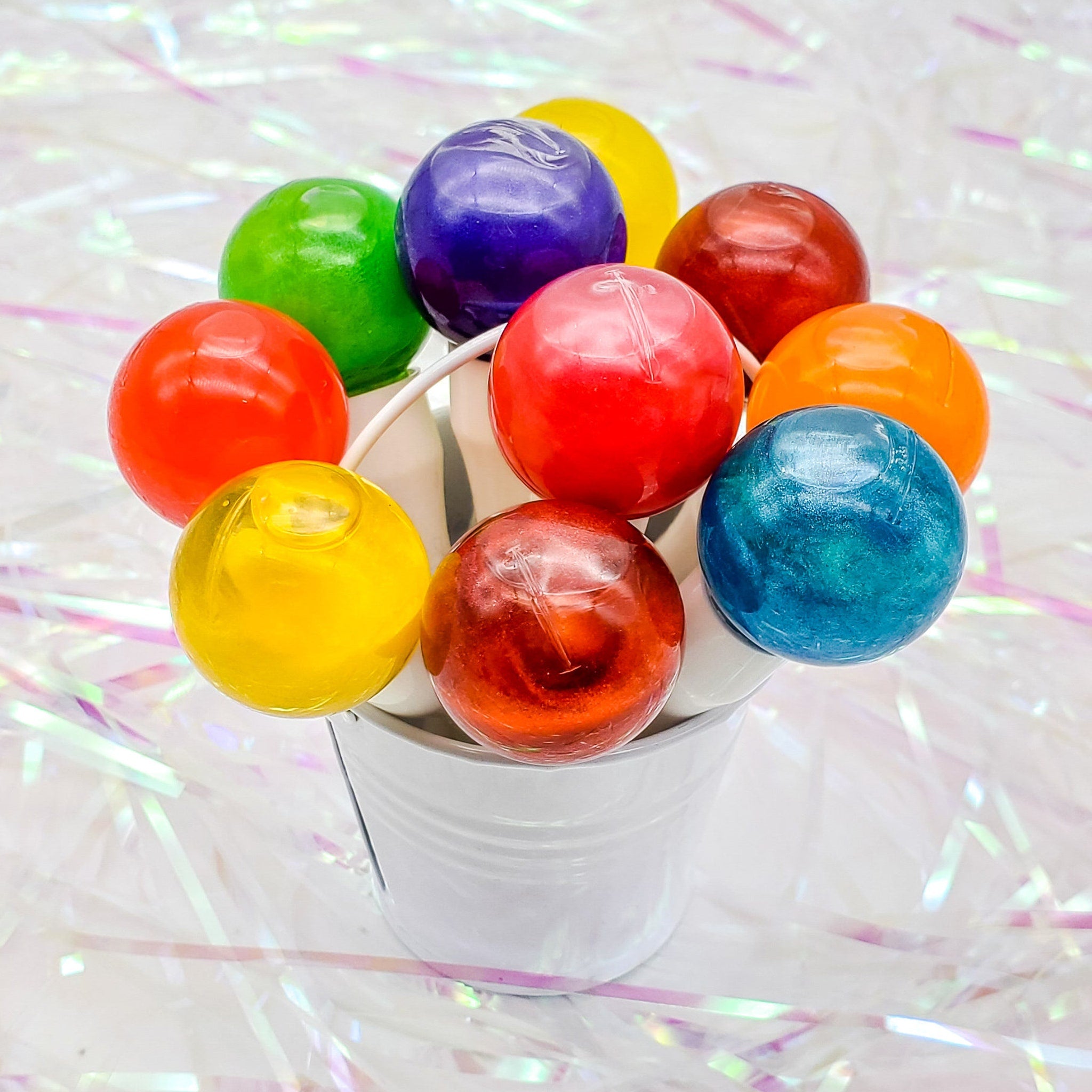 Lollipops in various colors, shiny, round, arranged in a white bucket on a reflective surface