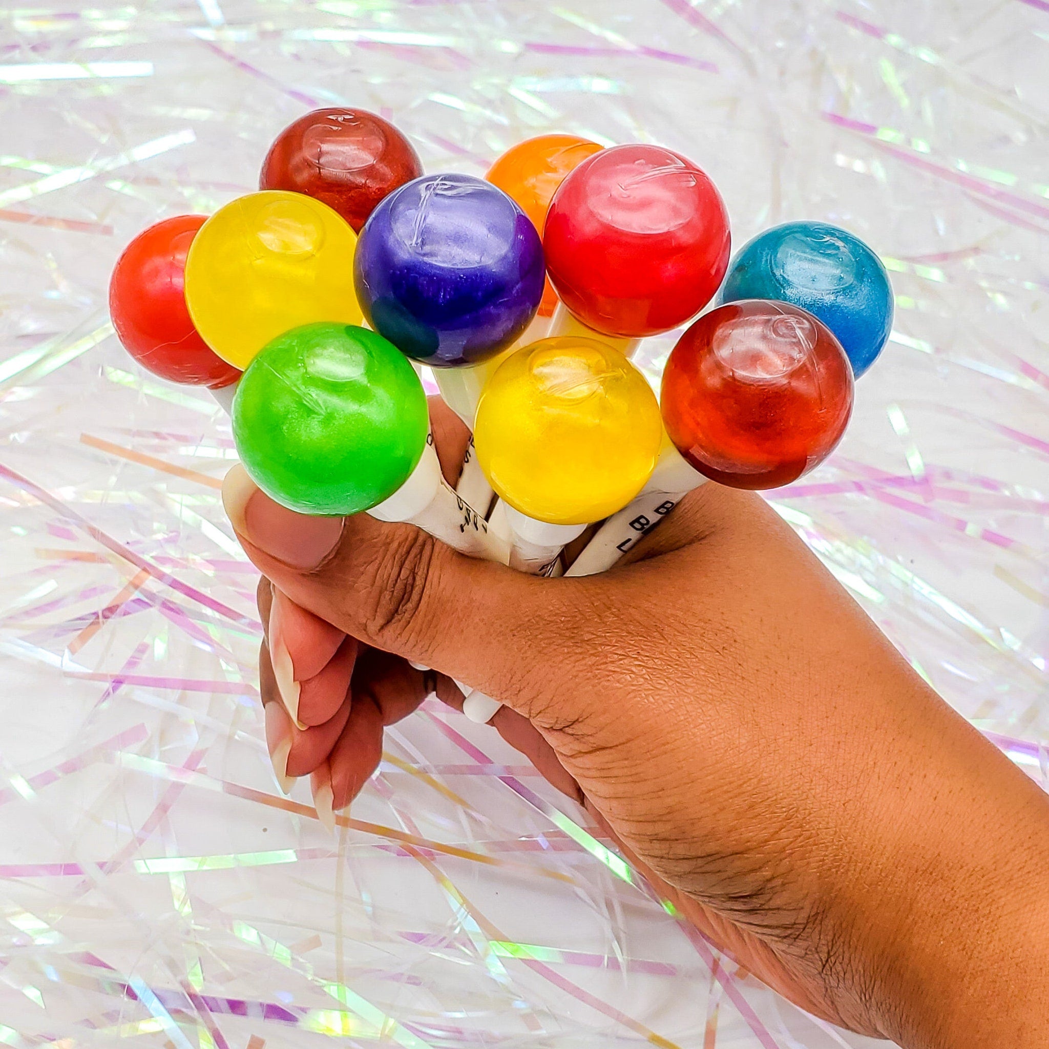 Lollipops in assorted colors, held in hand against a white and iridescent background