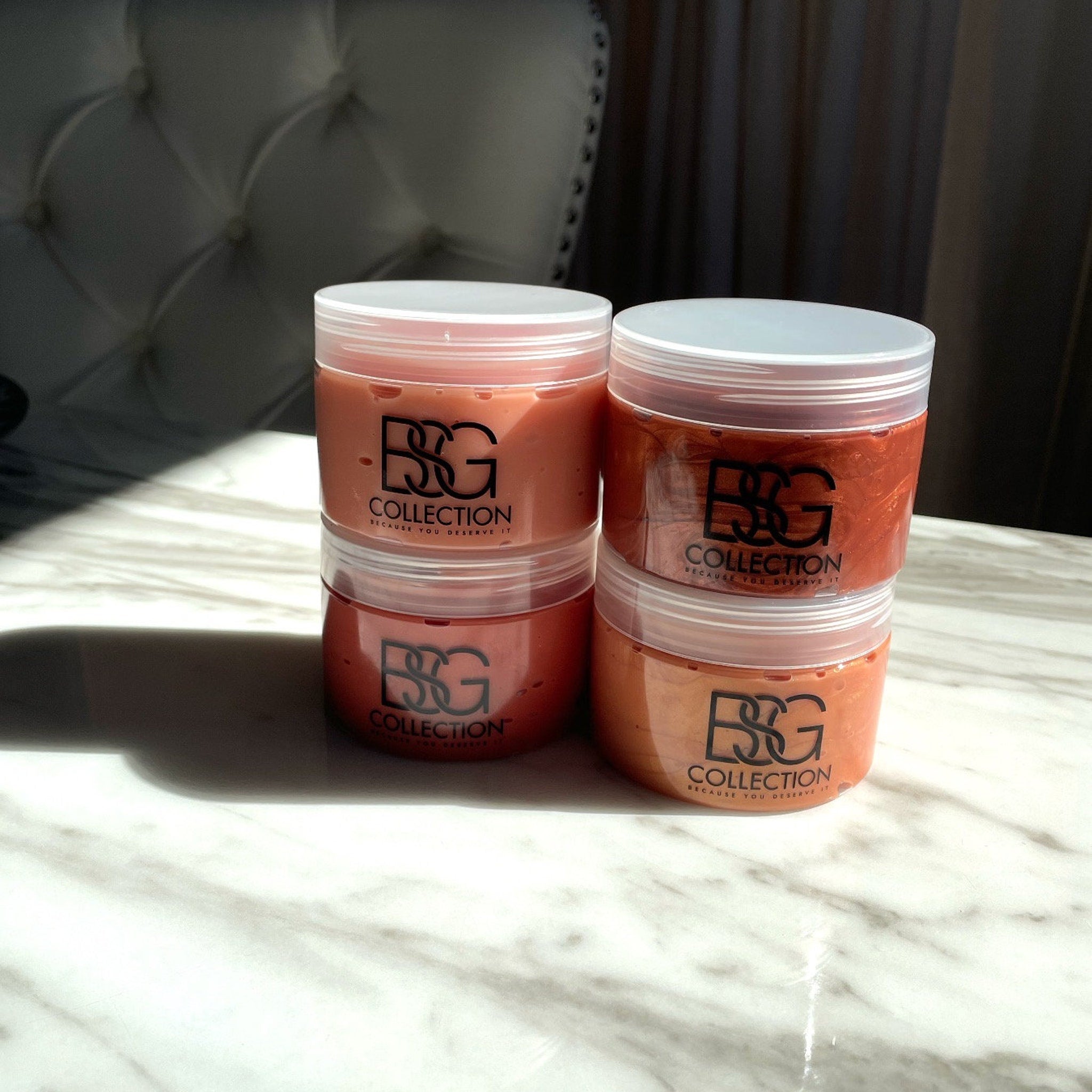 Cosmetic jars in stacked arrangement, with orange and red contents, white lids, and "BSG Collection" branding visible