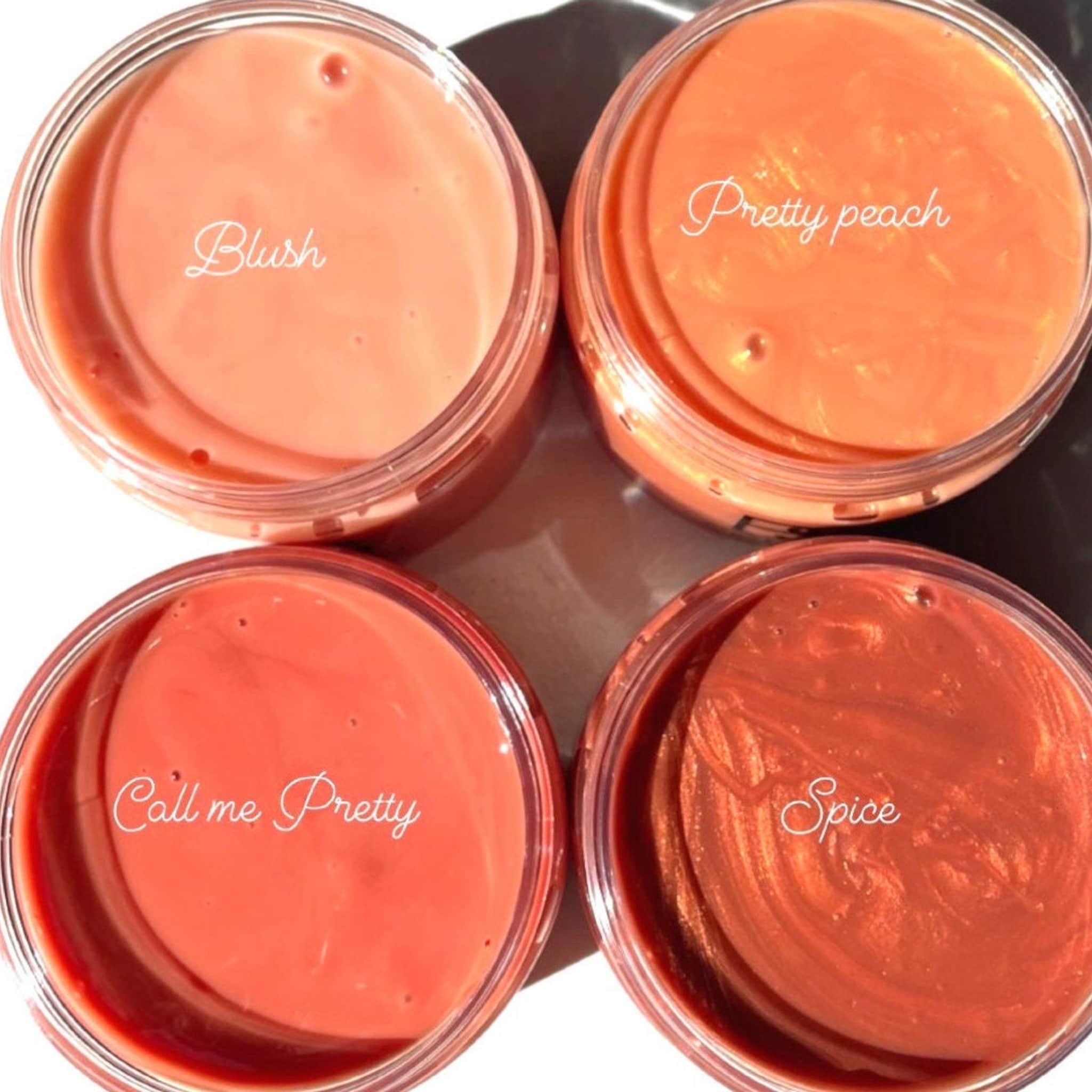 Lip gloss pots in peach, coral, and bronze shades with handwritten text labels