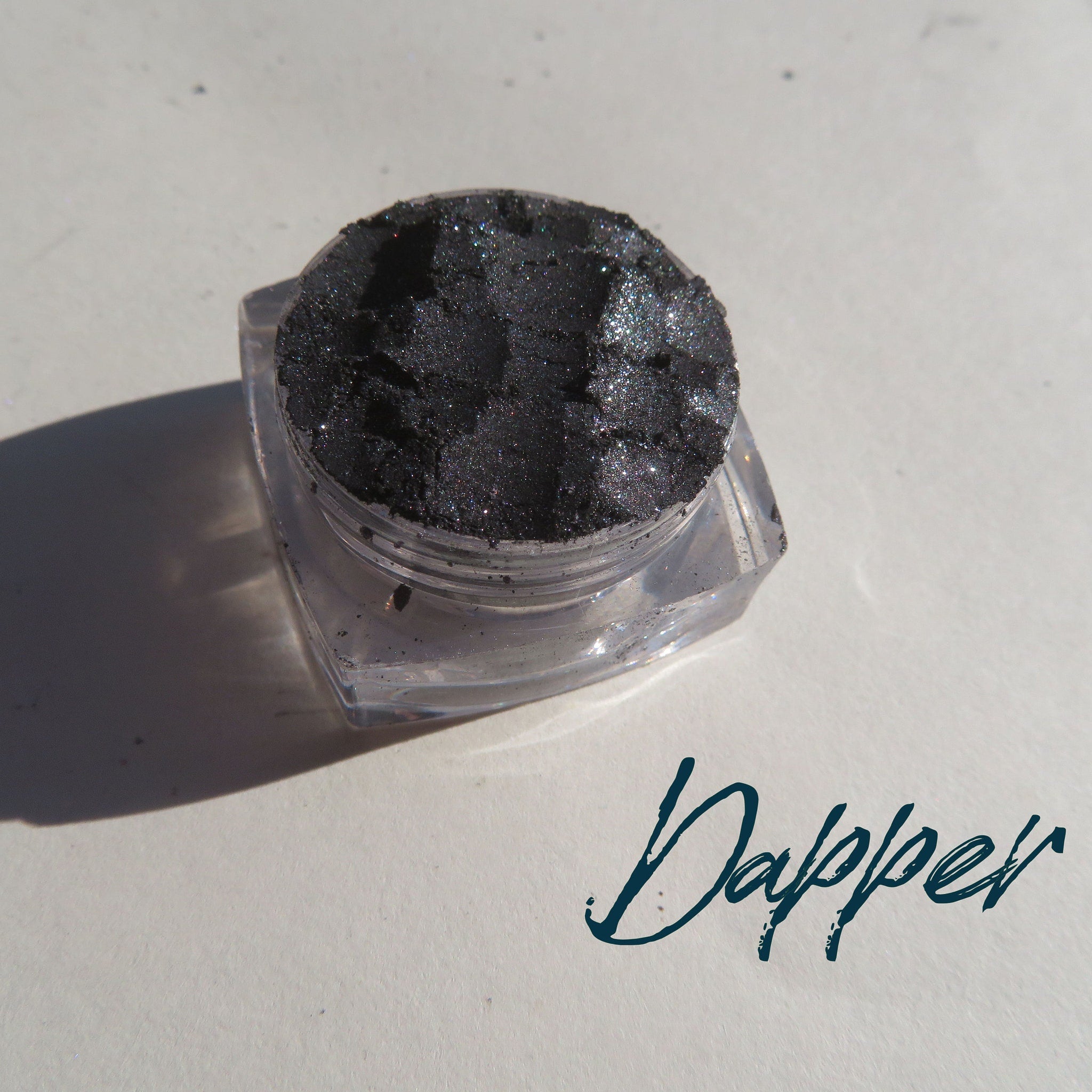 Black silver shimmer vegan mineral eyeshadow in loose powder form with cruelty-free label, displayed in open jar