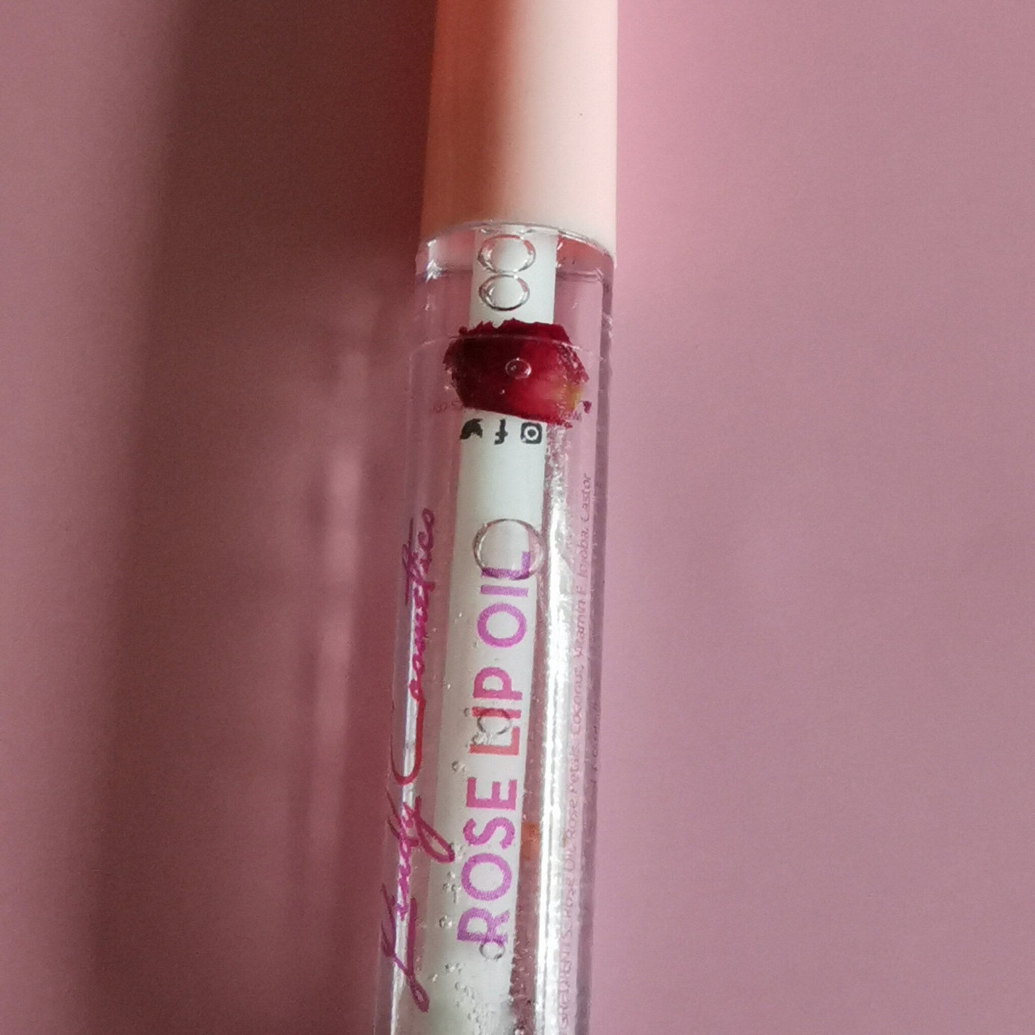 Rose lip oil in clear tube with pink cap and visible rose petals, Lady Cosmetics brand