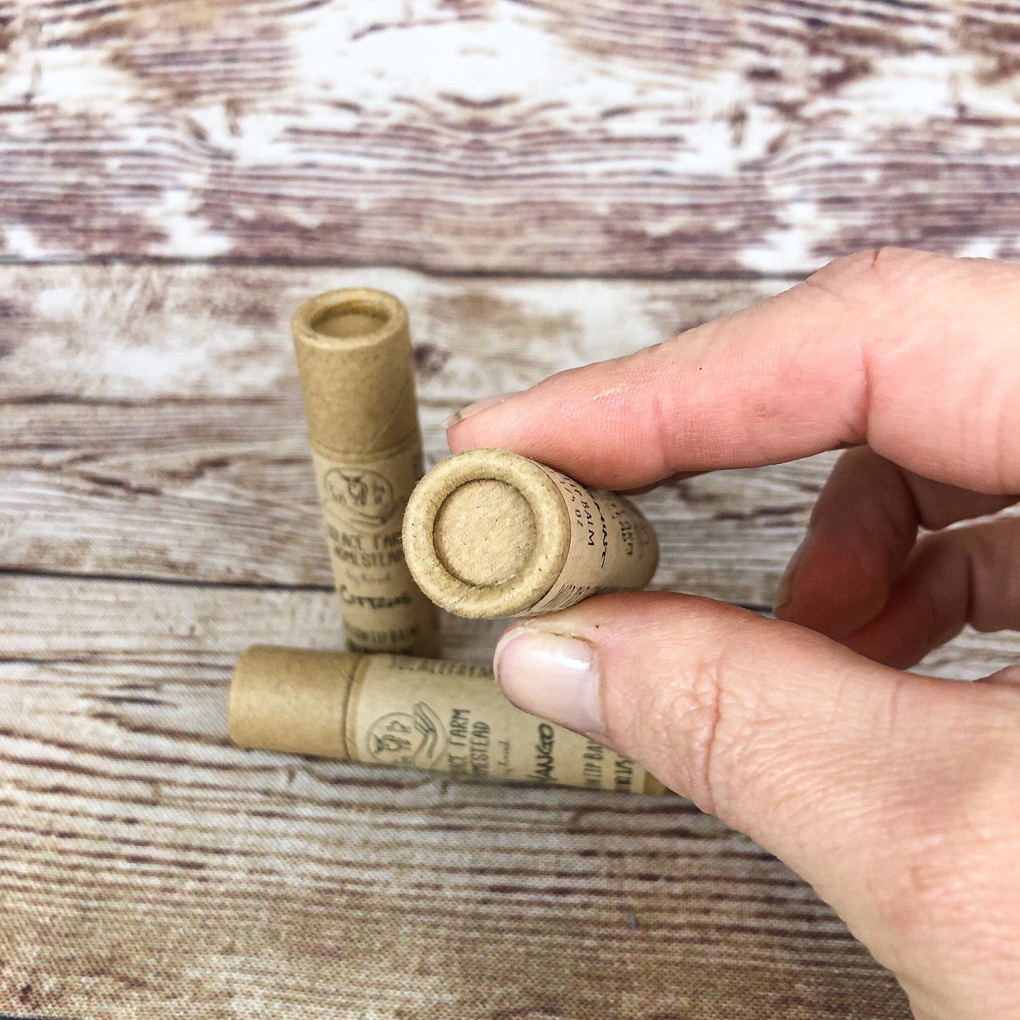 Lip balm tubes, brown cardboard, cylindrical shape, held by hand