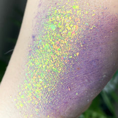 Iridescent glitter flakes on skin, purple and green color, cosmetic swatch