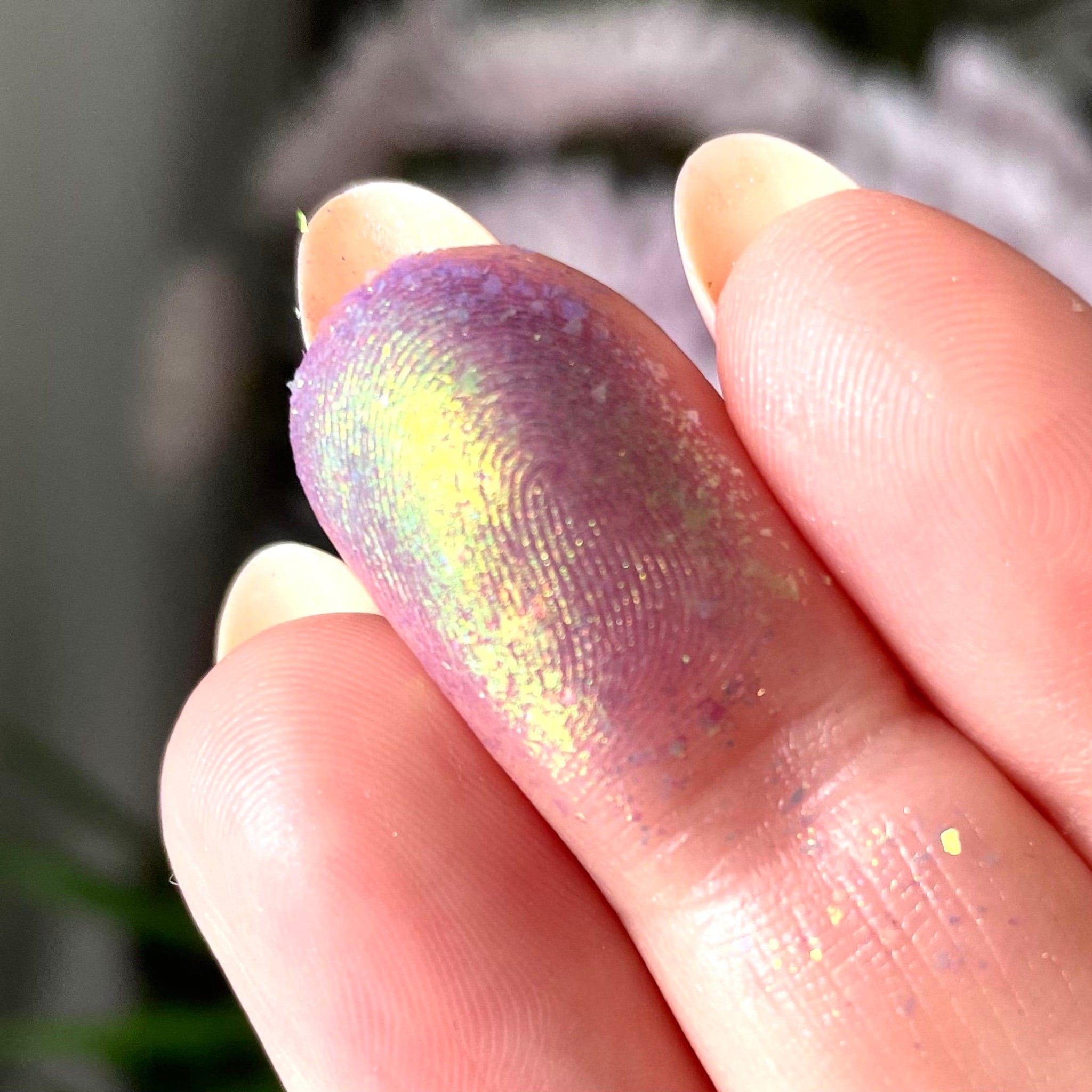 Iridescent eyeshadow swatch on finger, purple and yellow shimmer, close-up view