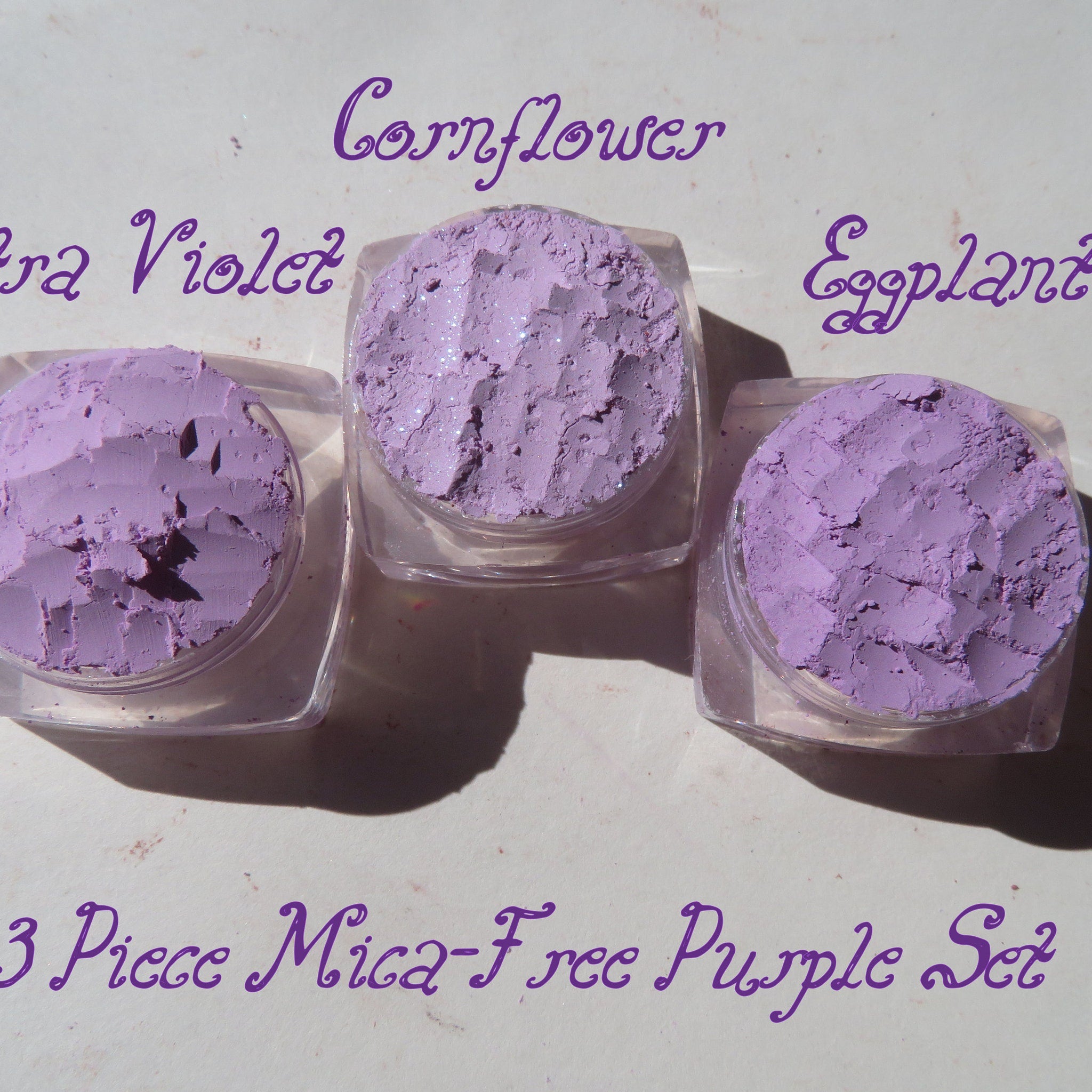 Three loose purple mica eyeshadow pigments in small jars with gold lids, vegan and cruelty-free mineral makeup.