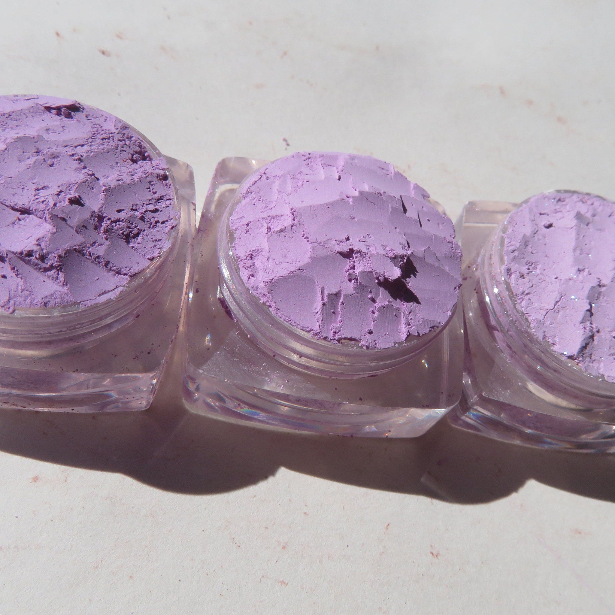 Close-up of three loose purple mica pigments in vegan mineral eyeshadow set, showcasing shimmer texture