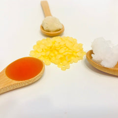 Ingredients in wooden spoons, orange liquid, yellow pellets, white solid, natural wood spoons