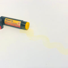 Lip balm tube with black and yellow label, yellow balm, and spilled liquid on white surface