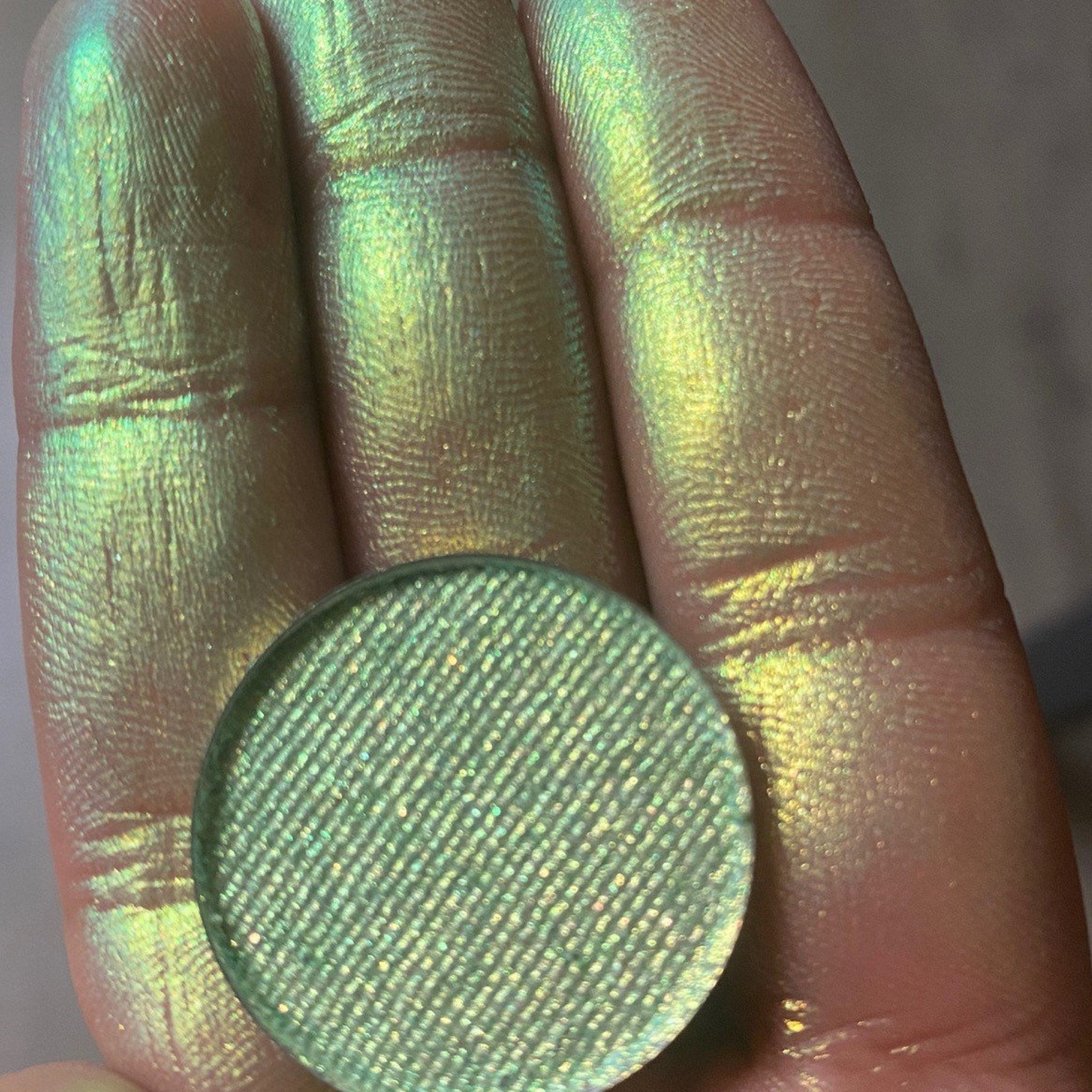 Close-up of fingertips applying multichrome eyeshadow with shimmering color shift effect on eyelid