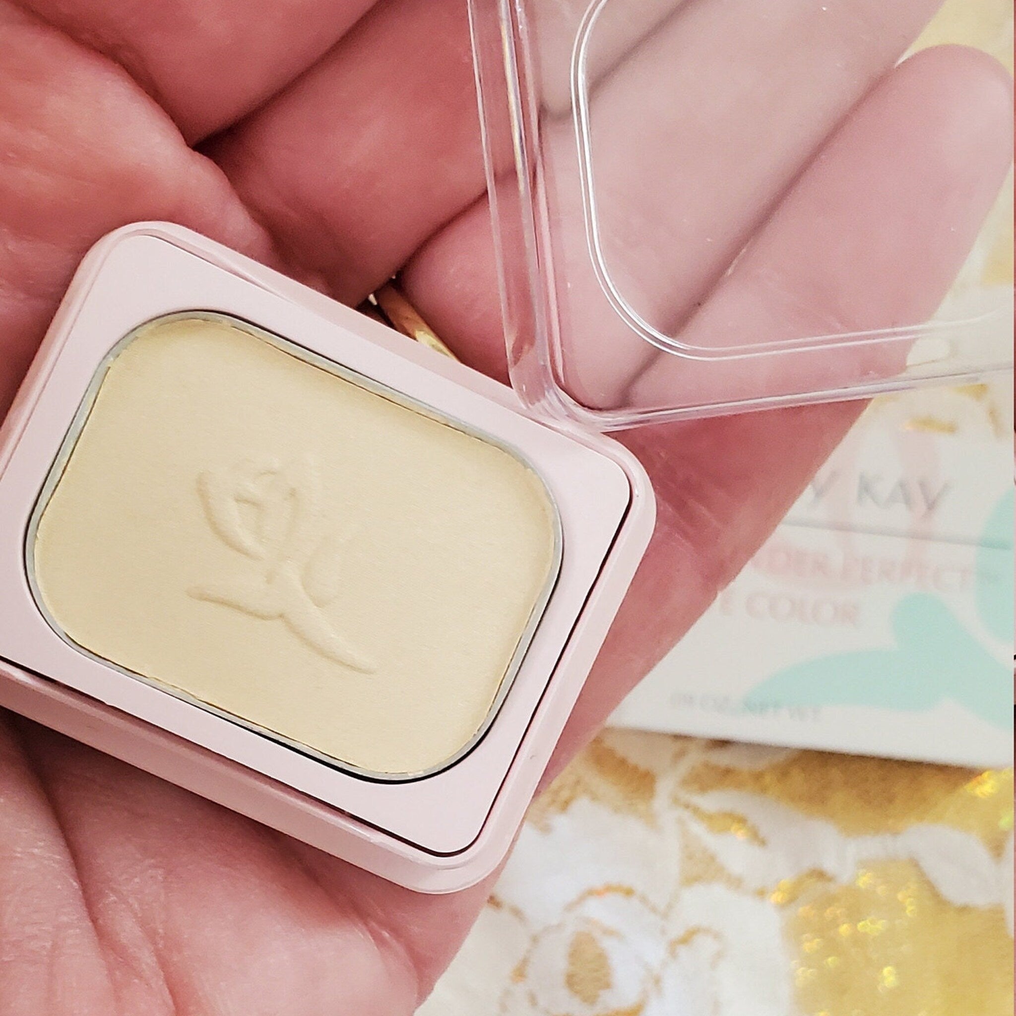 Powder compact, light pink case with pale yellow powder, clear lid open, Mary Kay brand visible