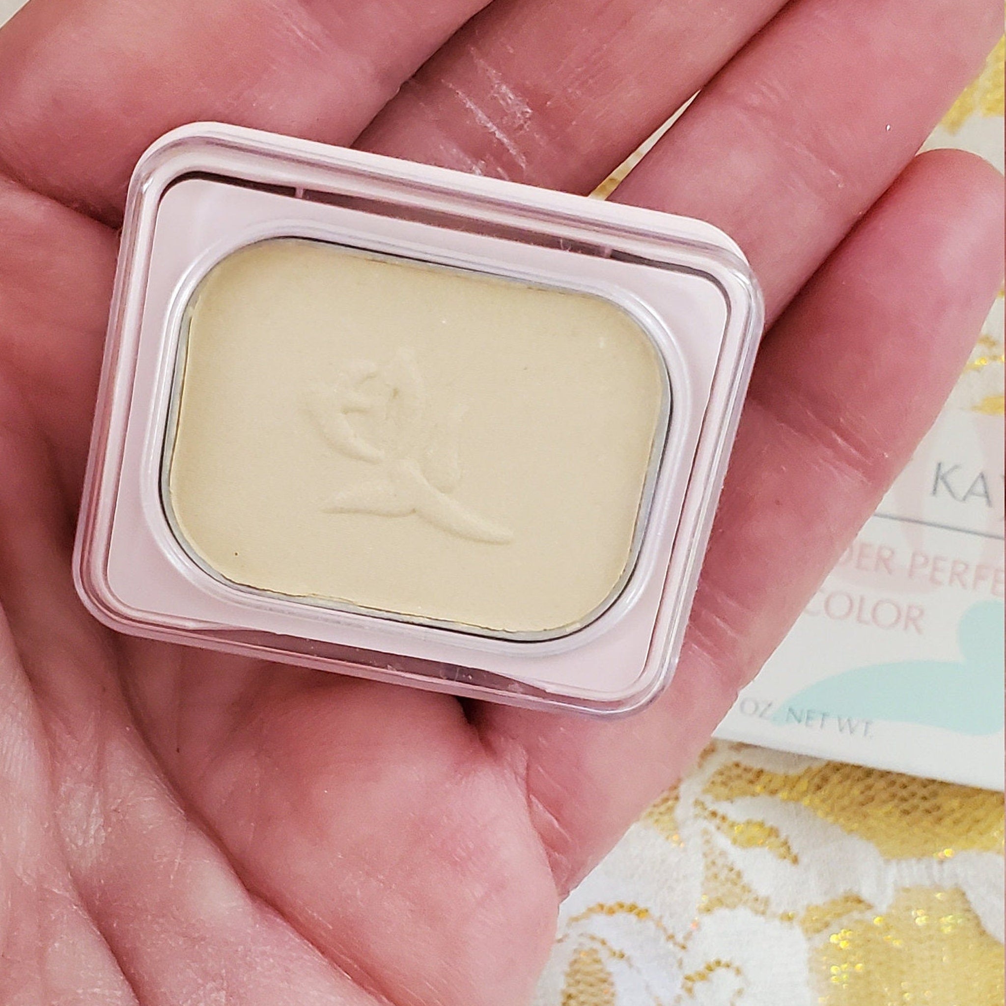 Powder compact with light yellow powder, pink rim, held in hand