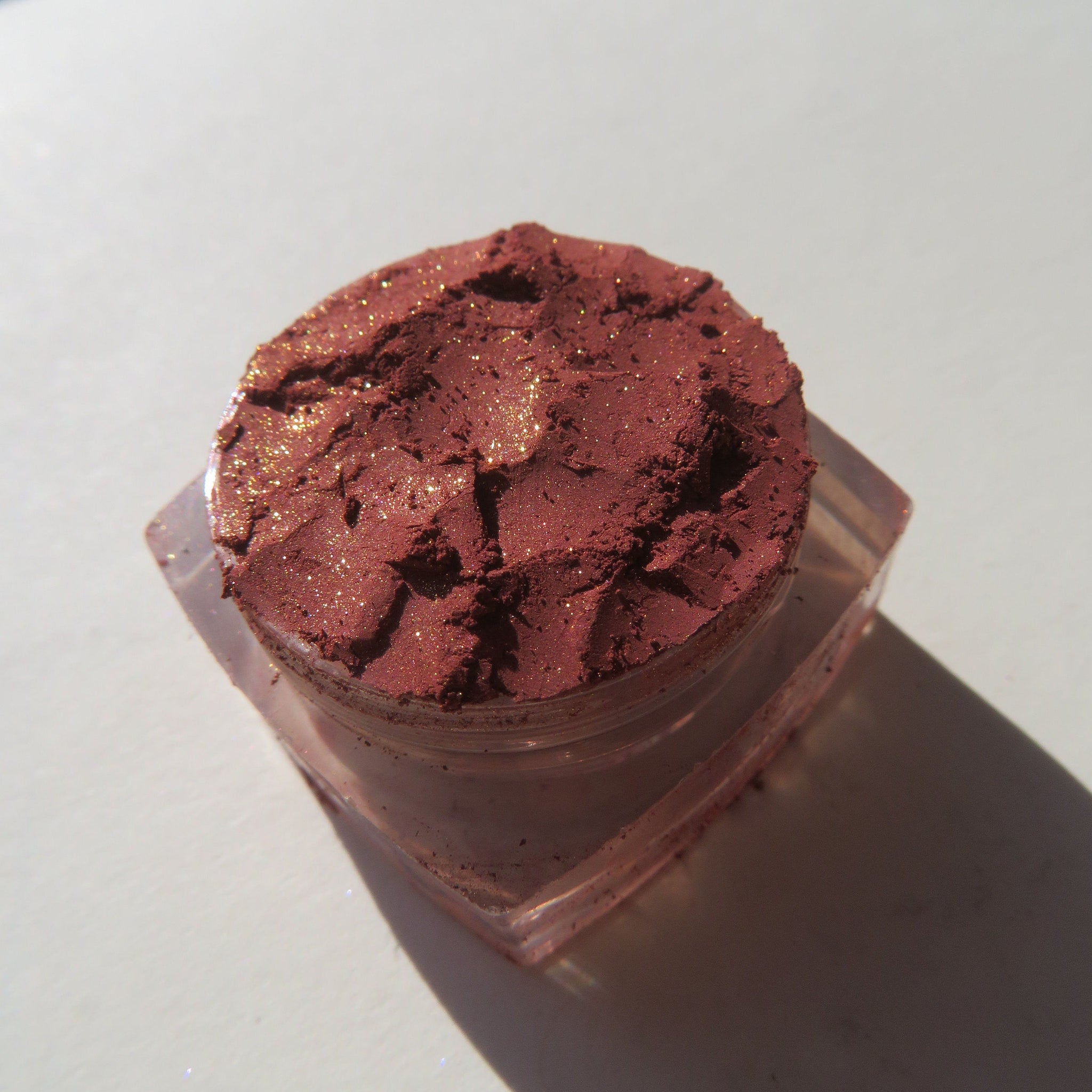 Close-up of loose brick red orange shimmer eyeshadow pigment with metallic sparkle