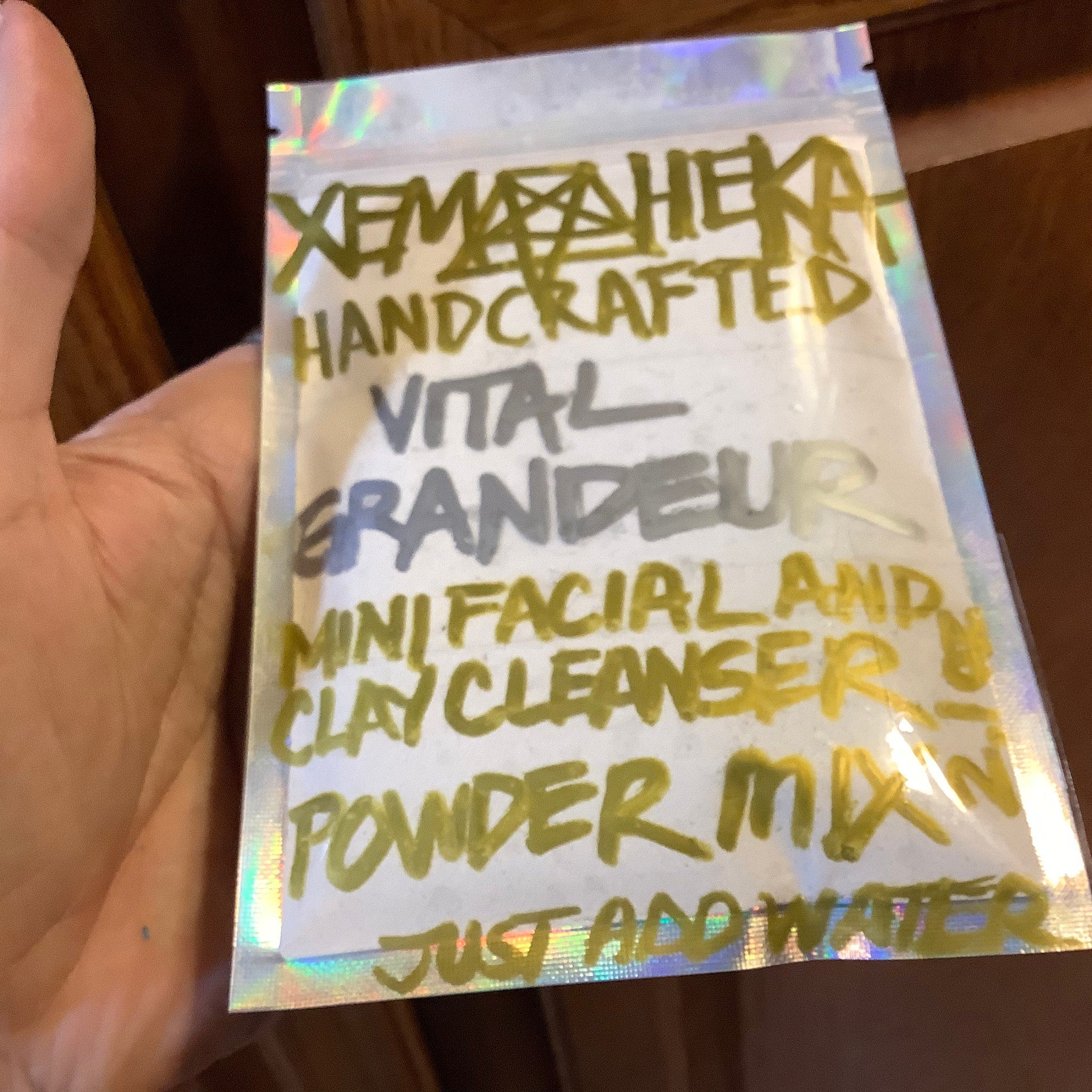 Facial cleanser packet with holographic foil, clear plastic, and handwritten text in gold ink
