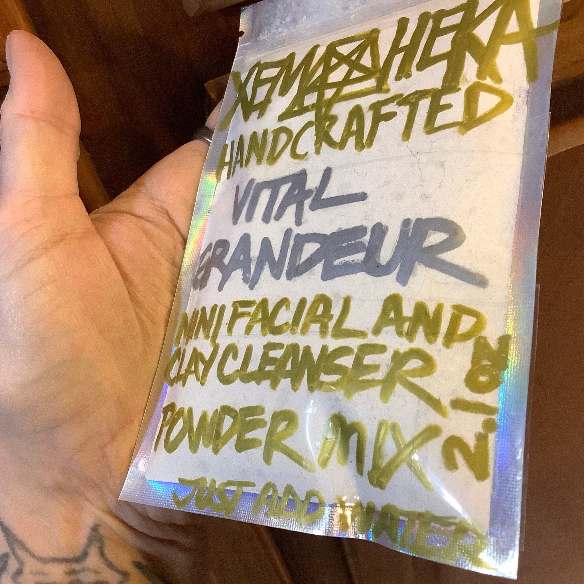 Facial cleanser powder mix in clear iridescent packet with handwritten text in green and grey