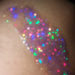 Glitter makeup swatch with multicolored sparkles on skin, iridescent and blurred effect