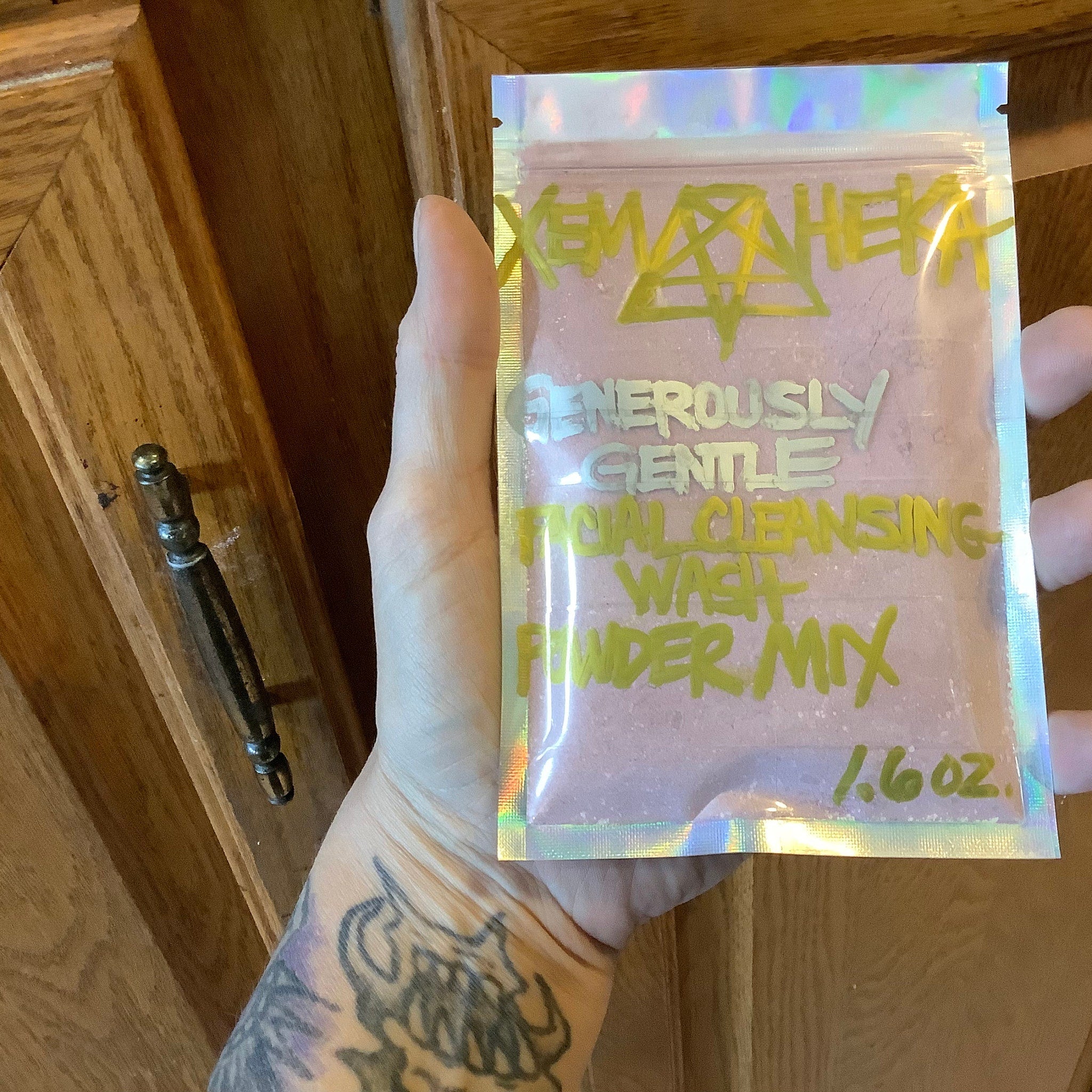 Facial cleansing powder mix in pink and holographic bag with green text, held in hand