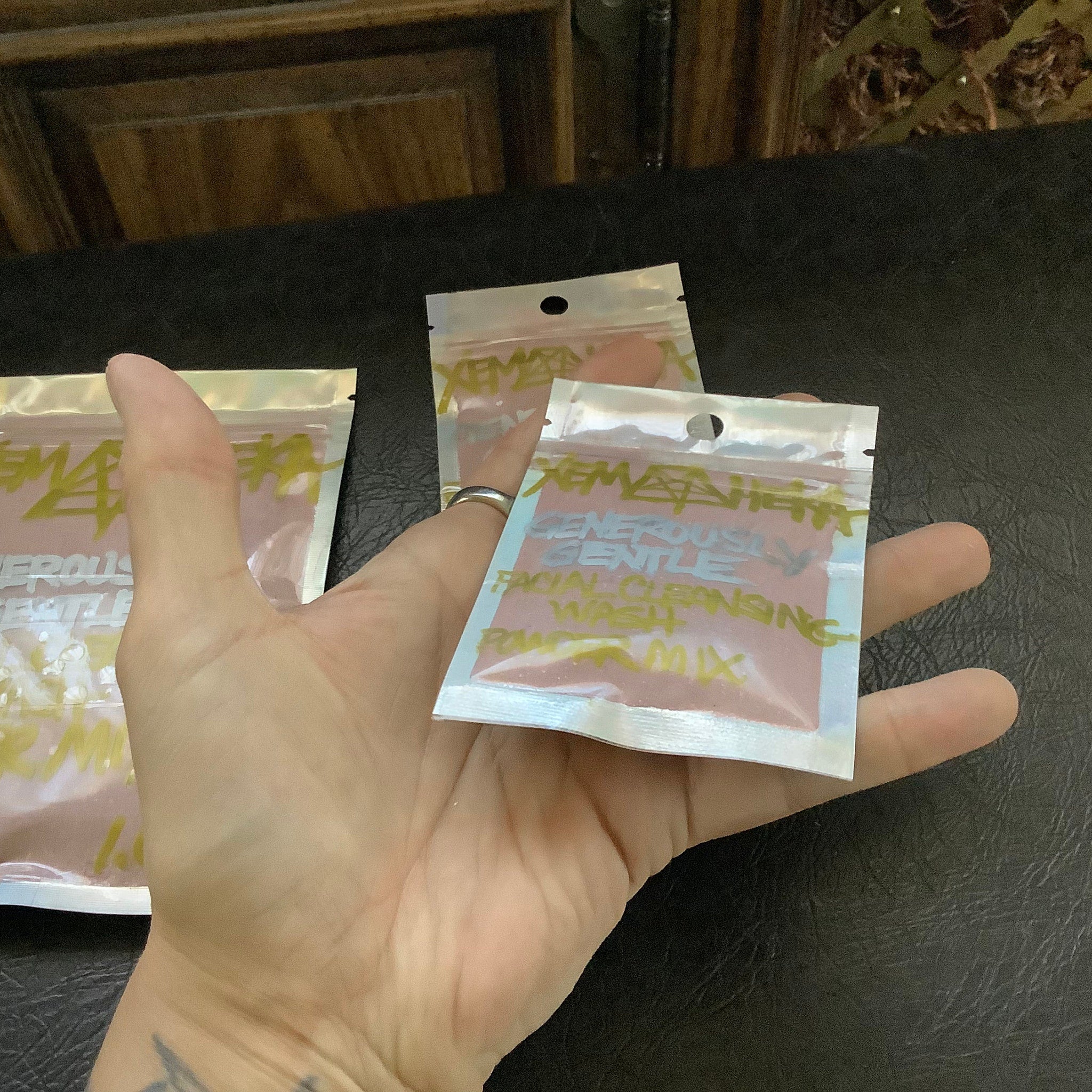 Facial cleansing powder packets in hand, pink powder, silver foil, handwritten text