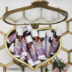 Lip balm tubes with white caps, purple label, in heart-shaped gold container, LAB SHAMAN visible