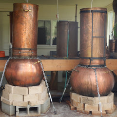 Copper stills with cylindrical and spherical shapes, sitting on brick and cinder block bases, with chains