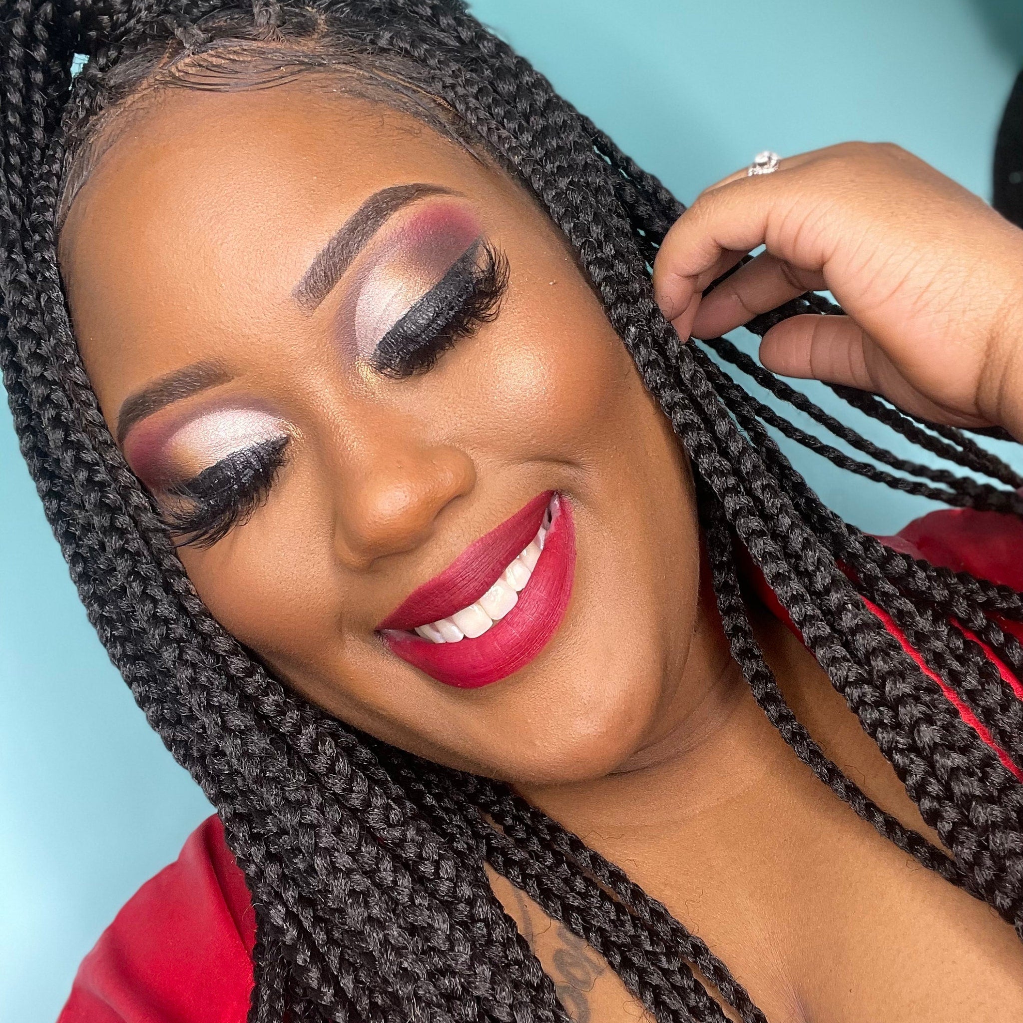 Braided hairstyle with black hair, red lips, and dramatic eye makeup smiling for a portrait