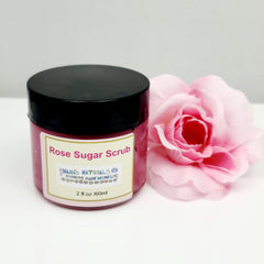 Rose sugar scrub jar with black lid, pink contents, and Nana's Naturals label, next to pink flower