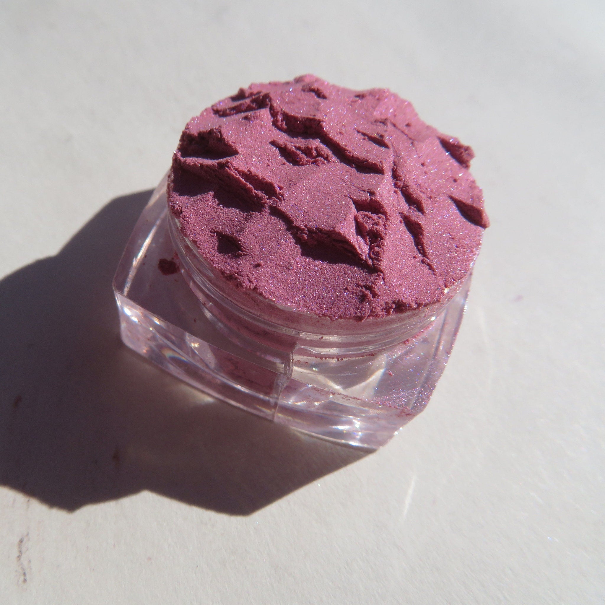 Close-up of Taylor loose mineral eyeshadow jar with pale pink shimmer powder visible inside
