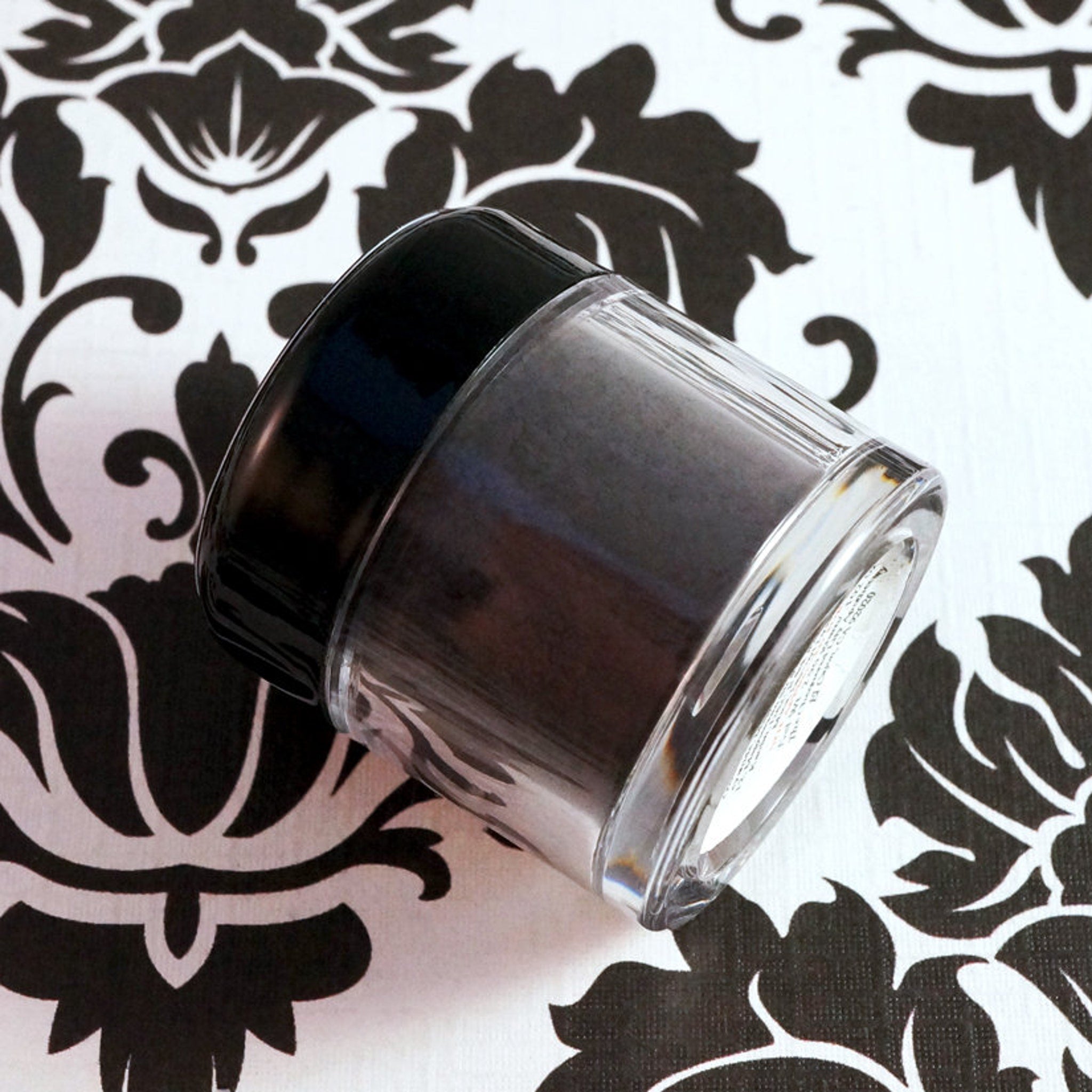 Dark purple loose mineral eyeshadow powder spilling from jar with metallic scoop on marble surface