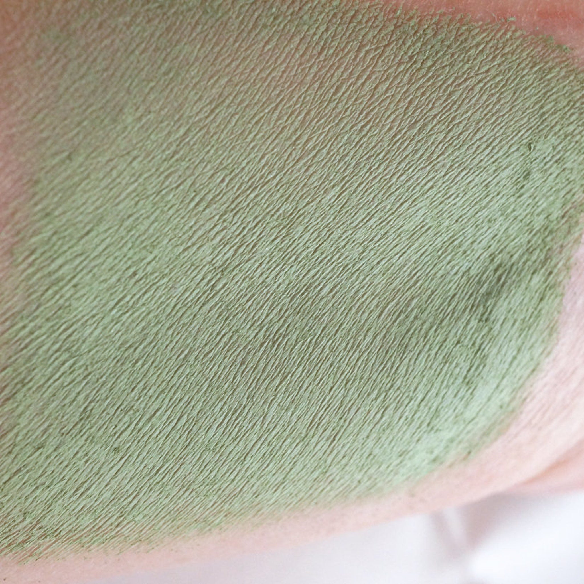 Close-up of matte sage green loose mineral eyeshadow with olive undertones in a sifter jar