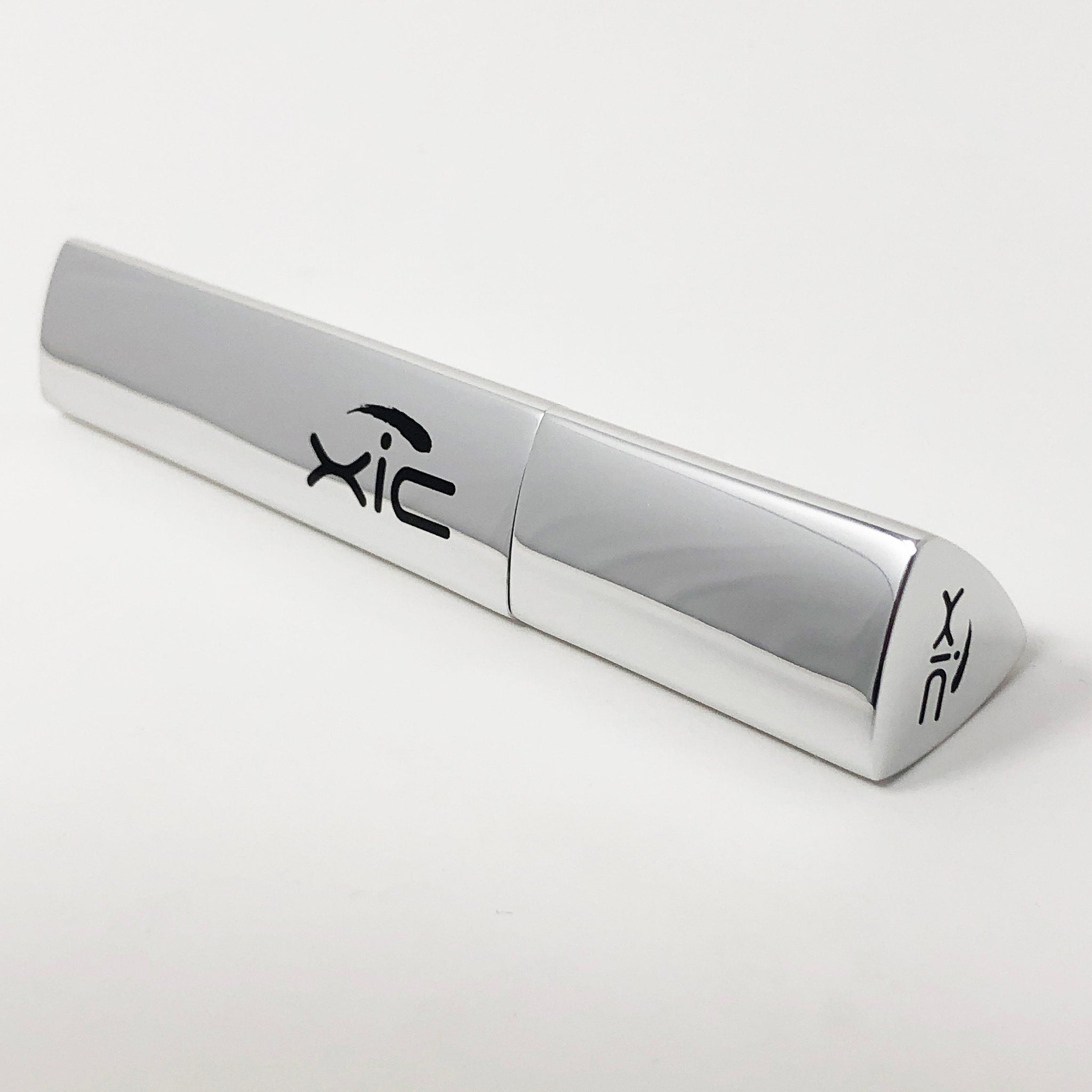 Silver tube with black "xic" logo, metallic finish, angled design on white background.