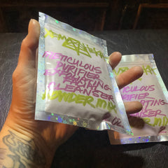 Facial cleanser packets with pink and green text on holographic plastic, held in hand