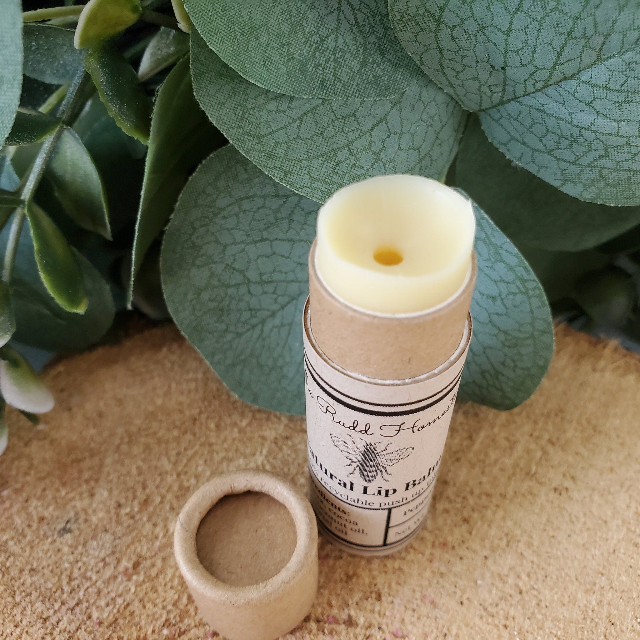 Lip balm in a brown paper tube with visible brand text, beige lip balm, and a separate cap
