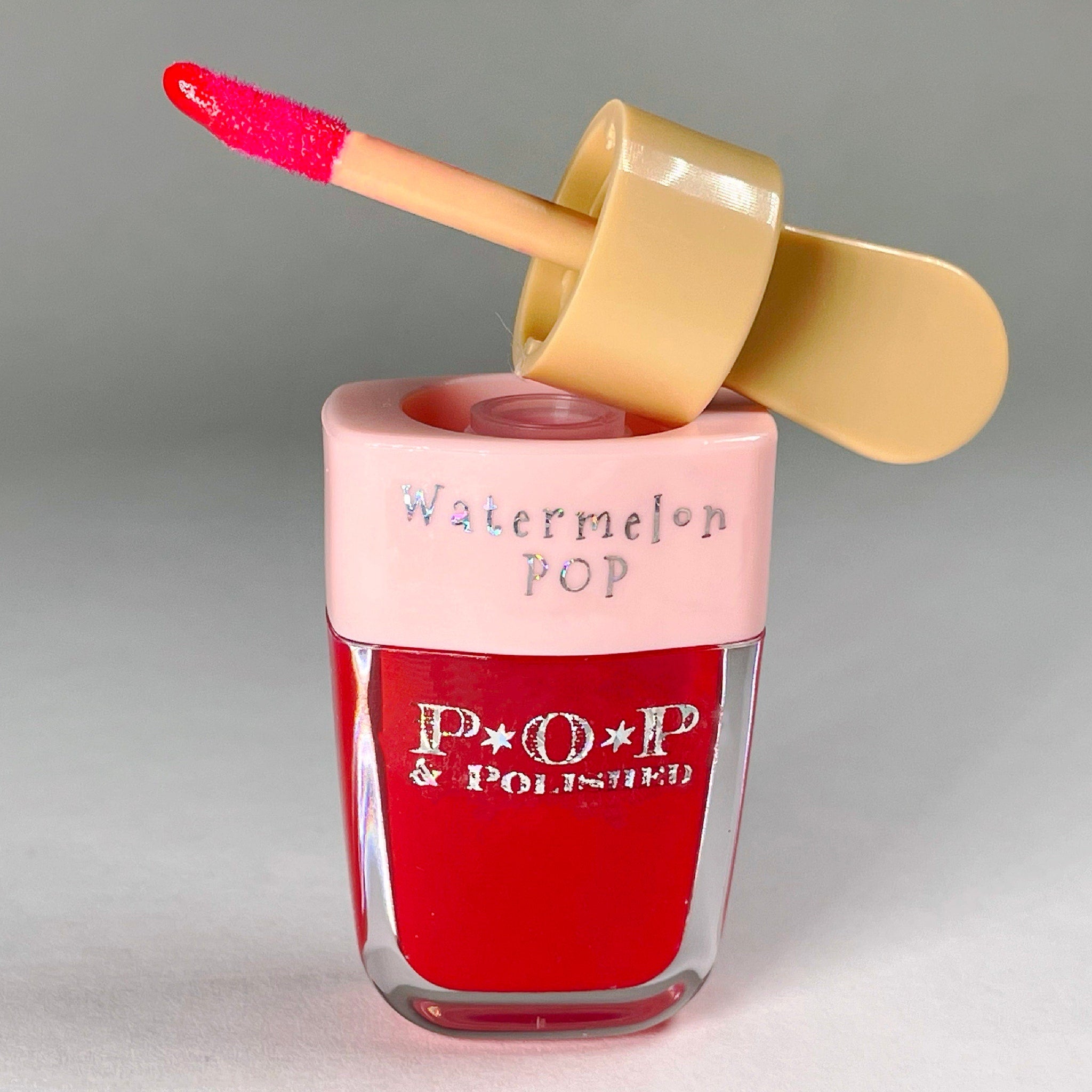 Lip gloss in red, pink, and clear glass with "Watermelon POP" text and applicator visible