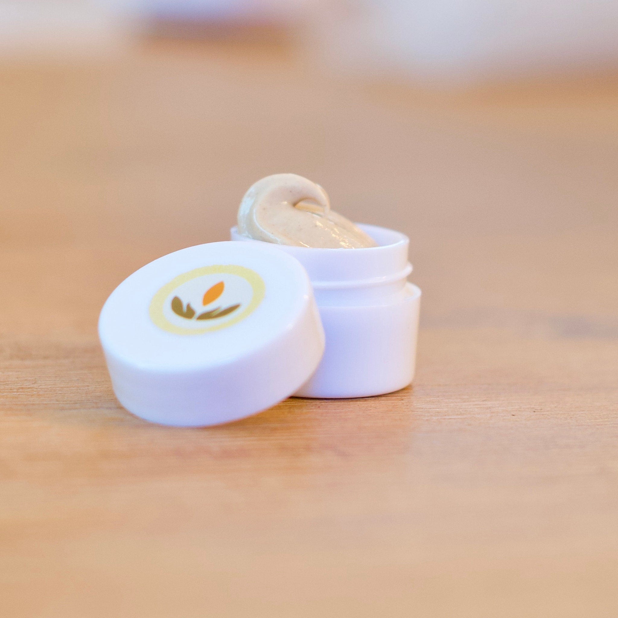Cream jar with white container, beige cream, and open lid on wood surface