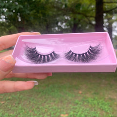 False eyelashes with black synthetic fibers in a pink box held by a hand