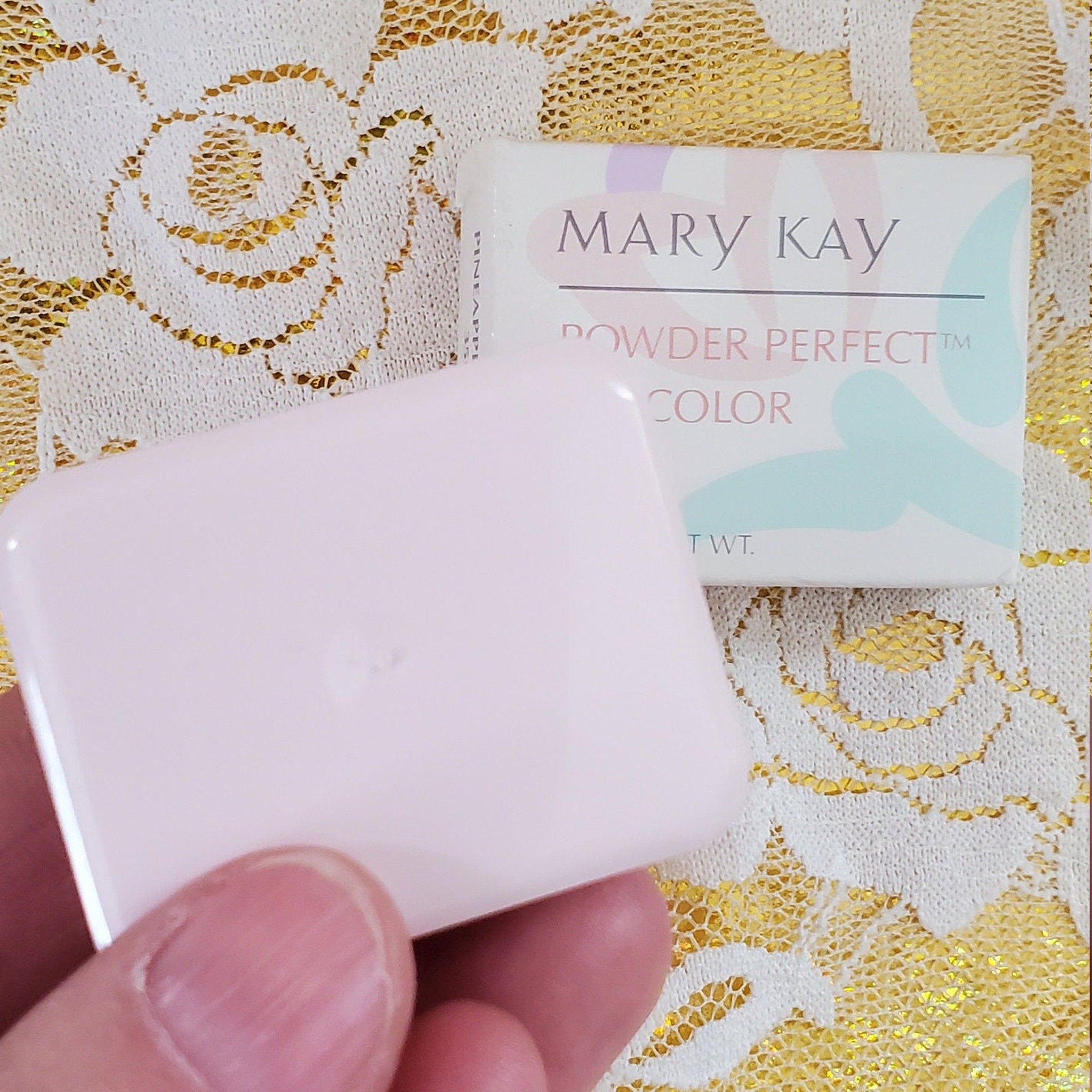 Mary Kay powder compact in light pink, white lace background, with text on box