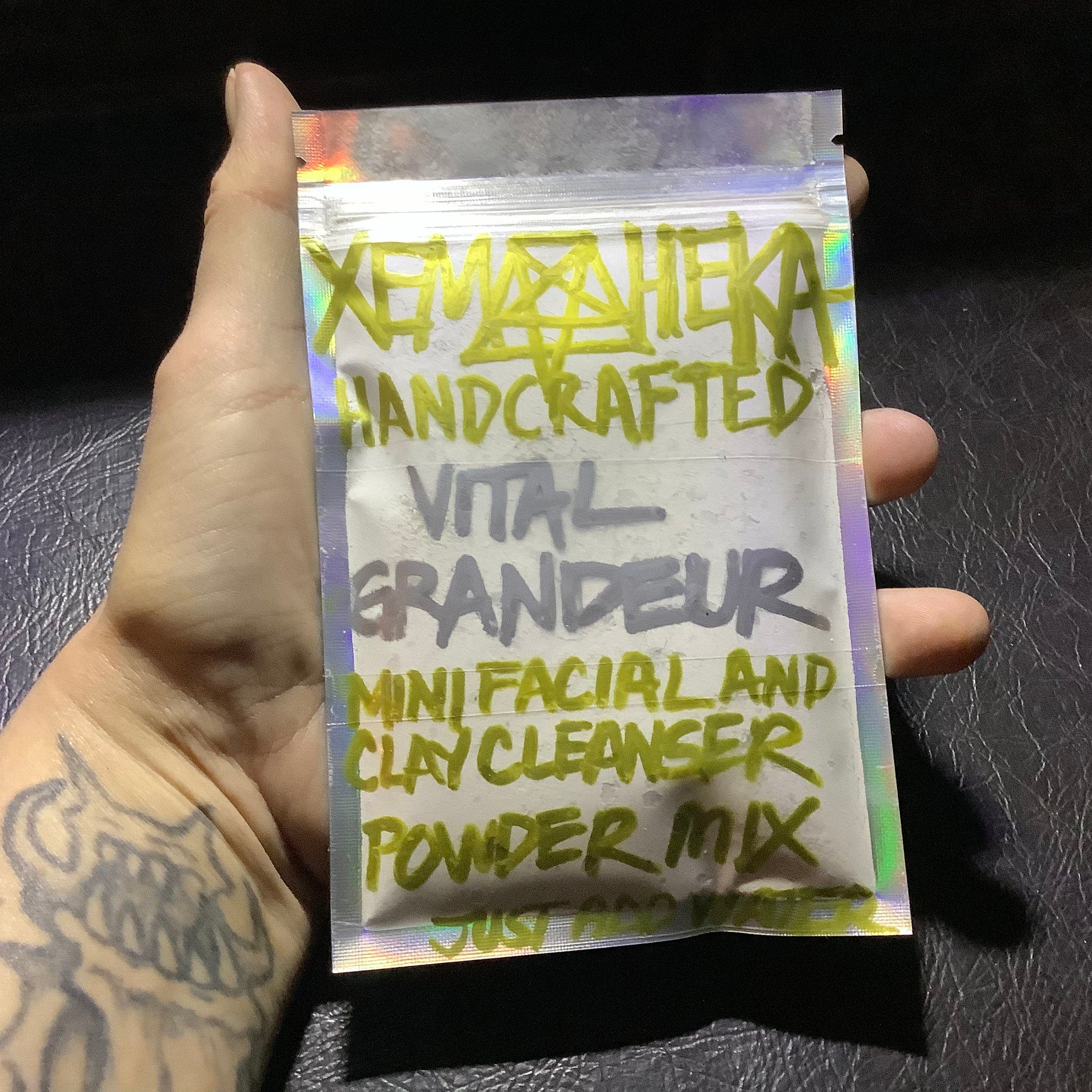 Facial clay cleanser powder mix in iridescent plastic pouch with handwritten green and gray text, held in hand