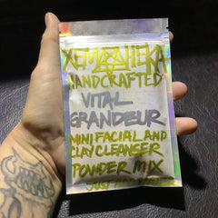 Facial clay cleanser powder mix in iridescent plastic pouch with handwritten green and gray text, held in hand