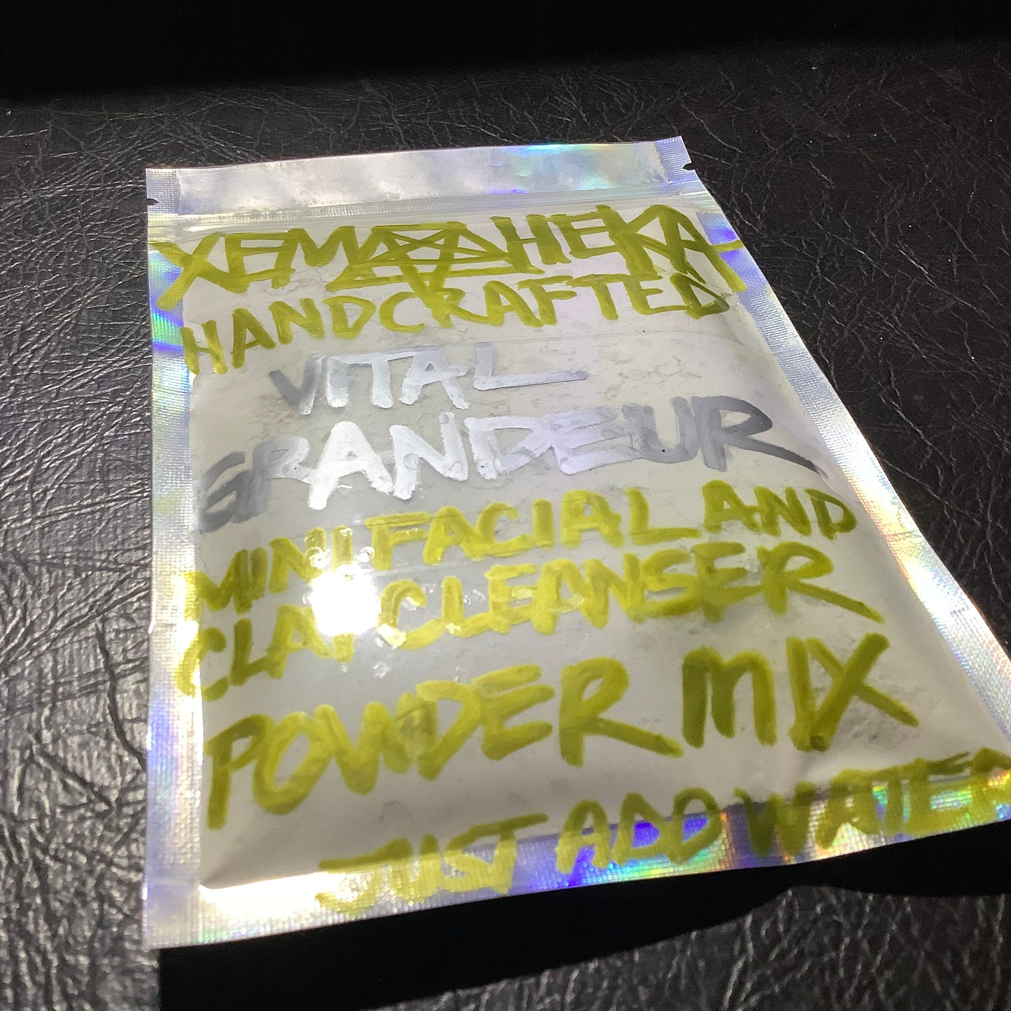 Facial cleanser powder mix in clear iridescent packet with handwritten yellow and silver text