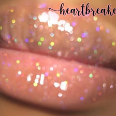Lip gloss with iridescent glitter, nude color, and "heartbreak" text overlay