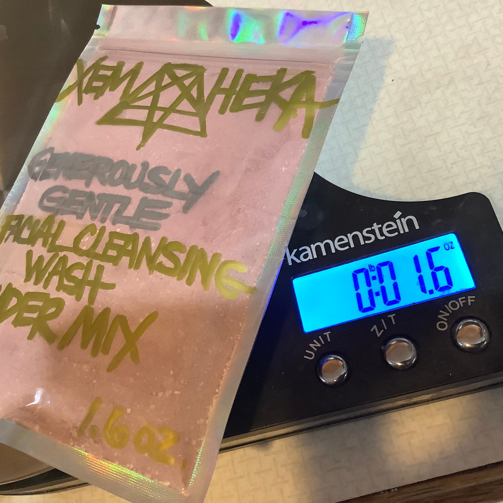 Facial cleansing powder mix in pink bag with green text, on scale, 1.6 oz weight shown