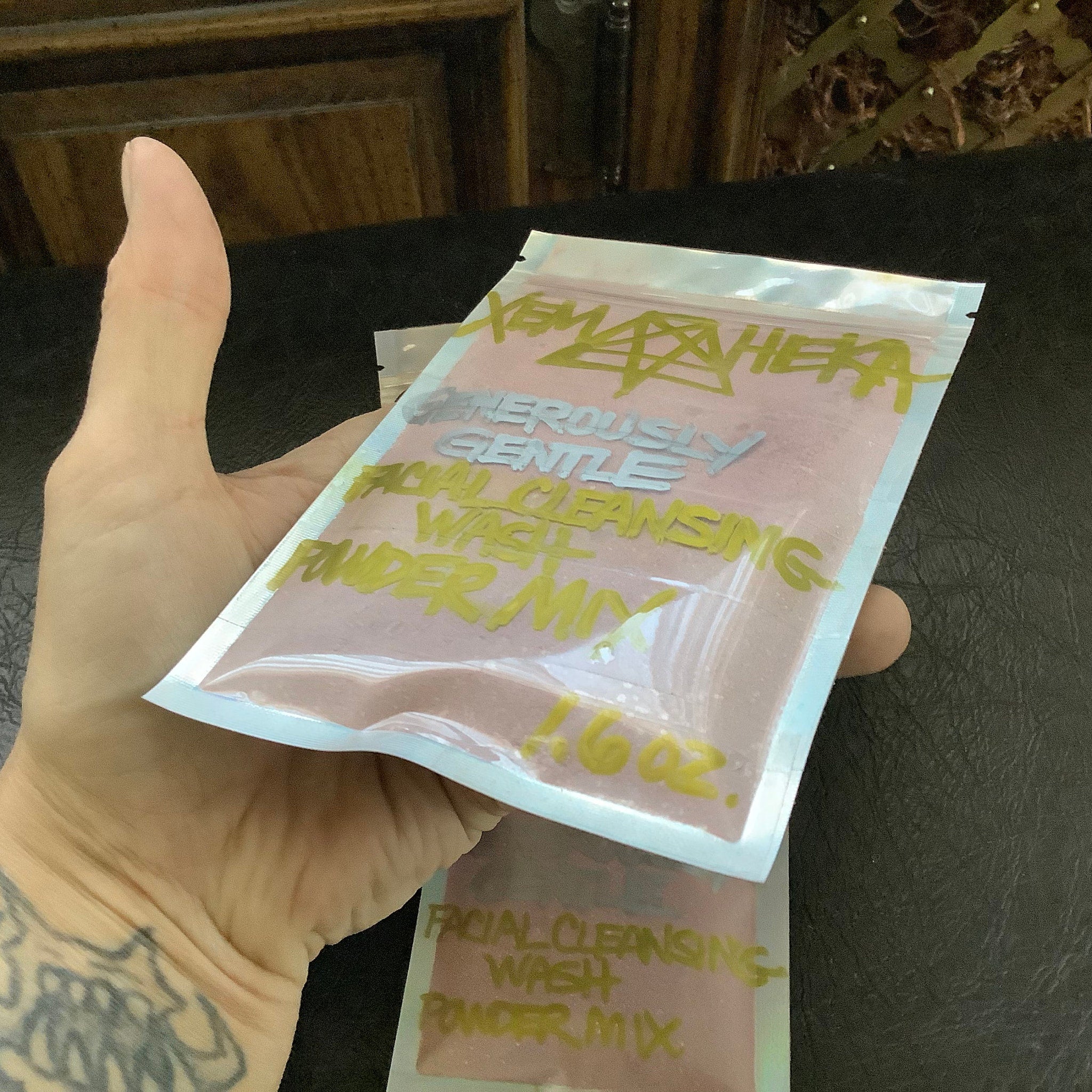 Facial cleansing powder mix in a clear plastic bag with pink powder and yellow text, held in hand