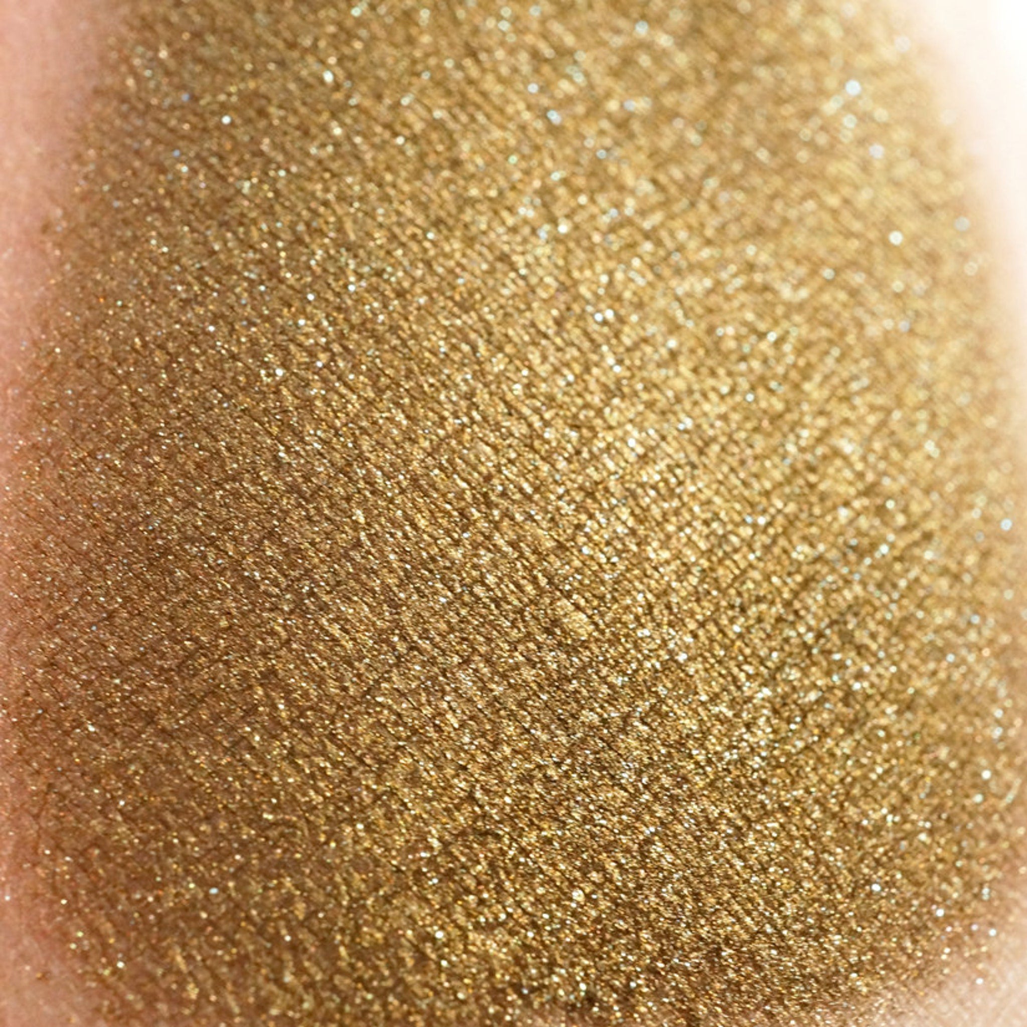 Bronze loose eyeshadow jar with gold and green glitter, showcasing spilled powder on marble surface
