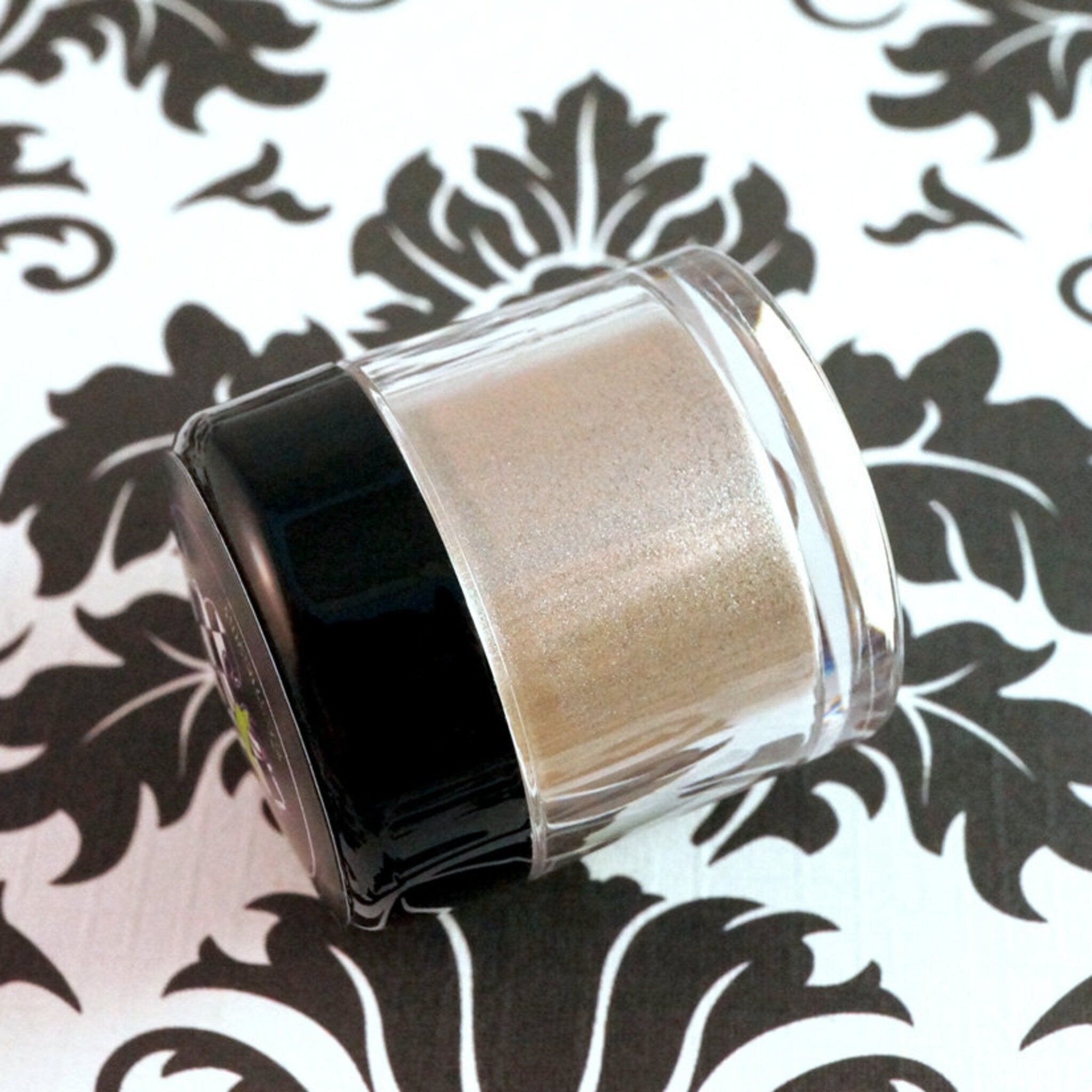 Side view of loose metallic taupe and champagne eyeshadow pigment with silver shimmer in open jar