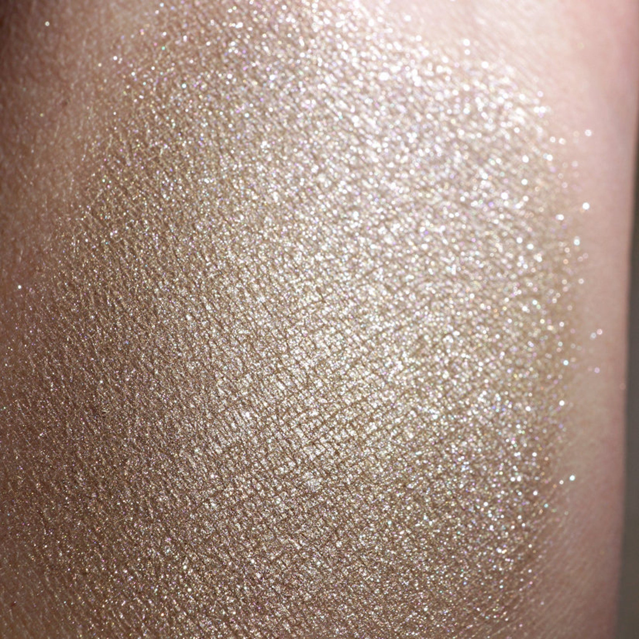 Close-up of loose metallic taupe and champagne eyeshadow pigment with silver shimmer particles scattered on skin