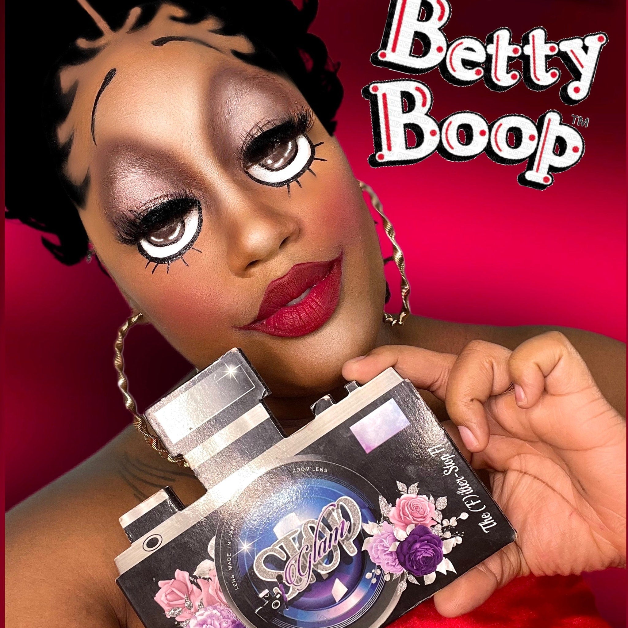 Betty Boop makeup with black and white cartoon style eyes and red lipstick, holding a black box with Glam text and floral design